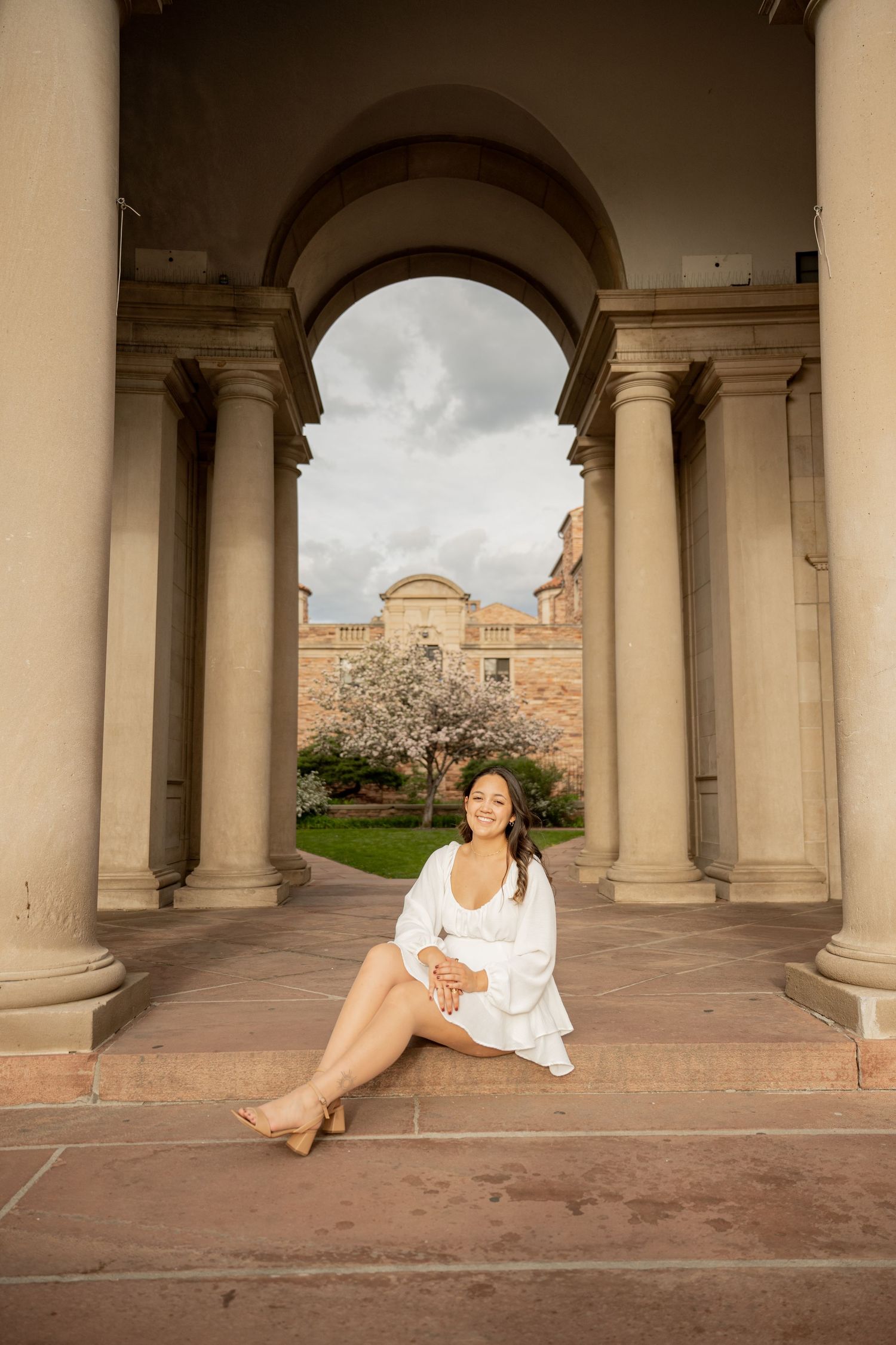 A person in white dress lounges elegantly under ornate stone archways and columns at a historic building.