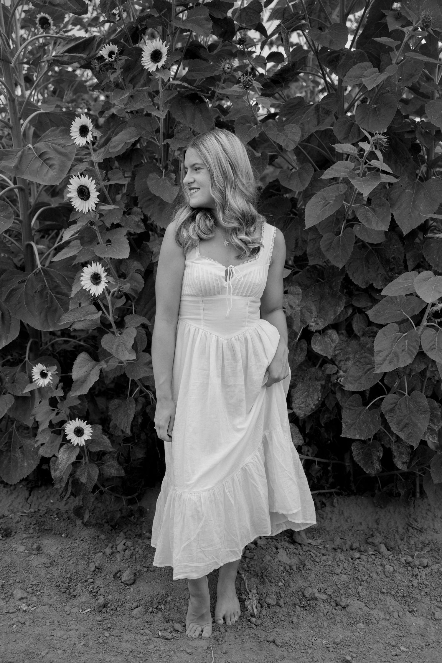 A series of black and white photos showing a person in a white dress standing among tall sunflower plants.