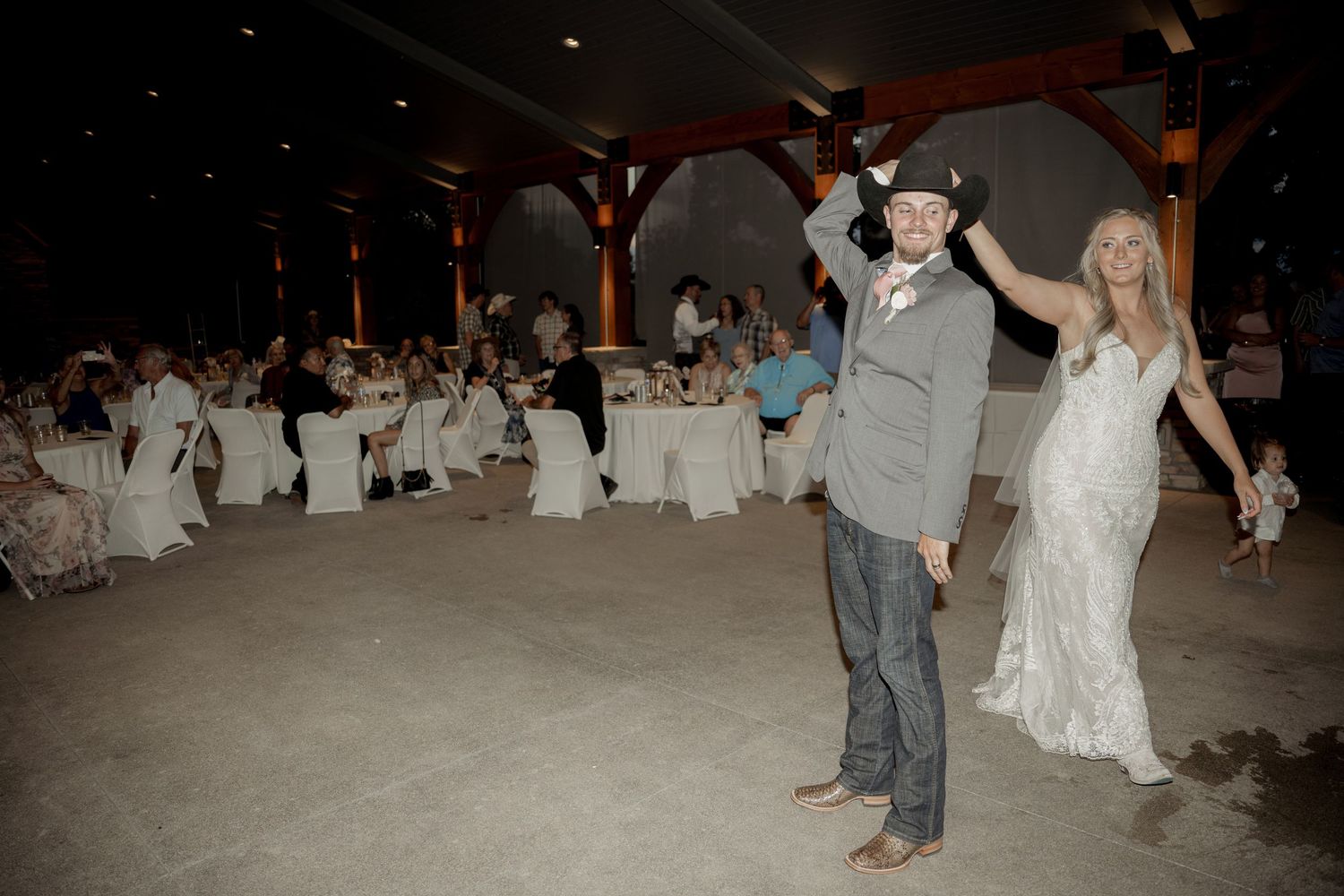A bride and groom perform their first dance surrounded by guests at a wedding reception.
