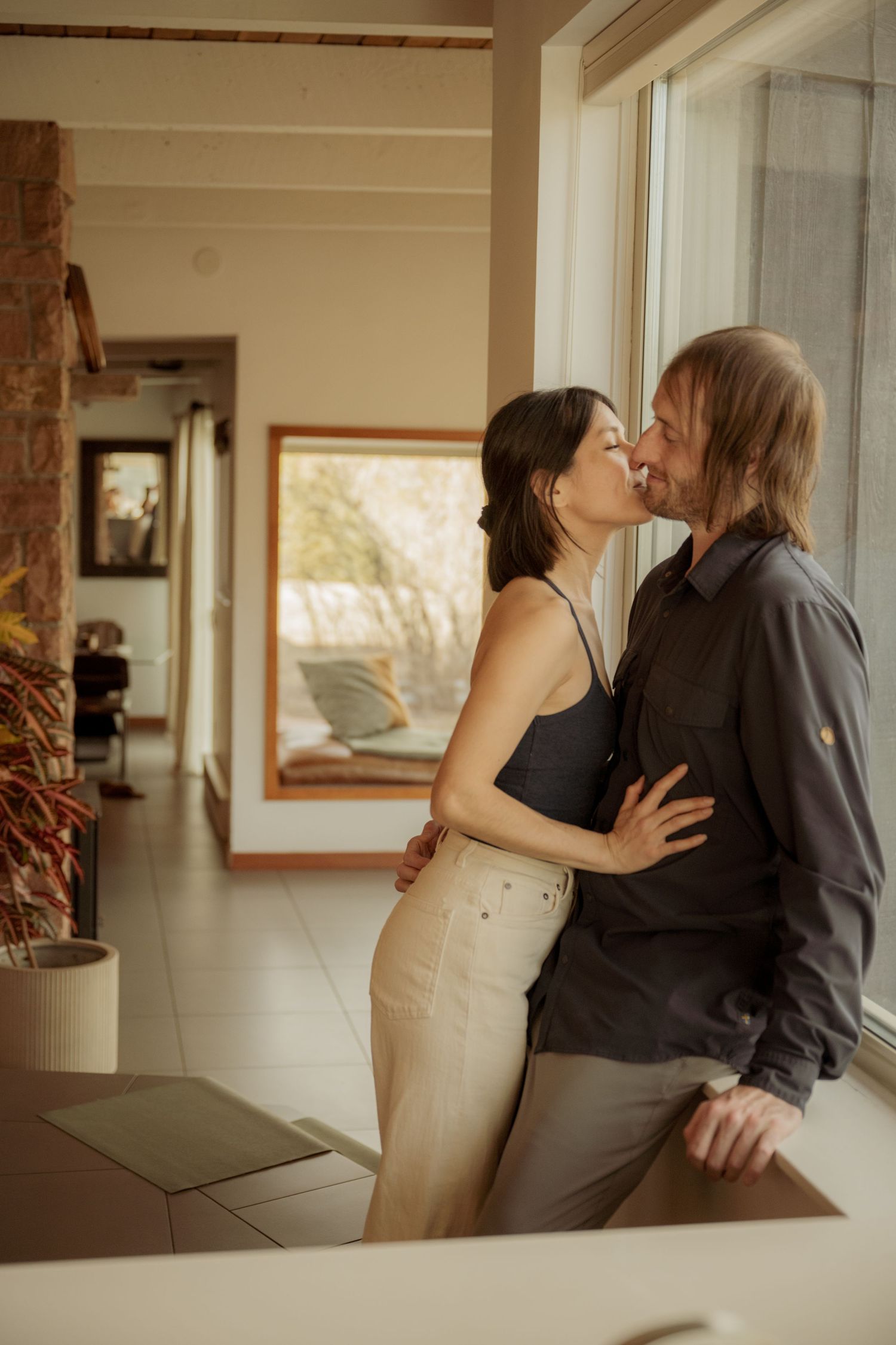 A romantic couple shares an intimate moment in a sunlit room with modern minimal decor and brick accent wall.