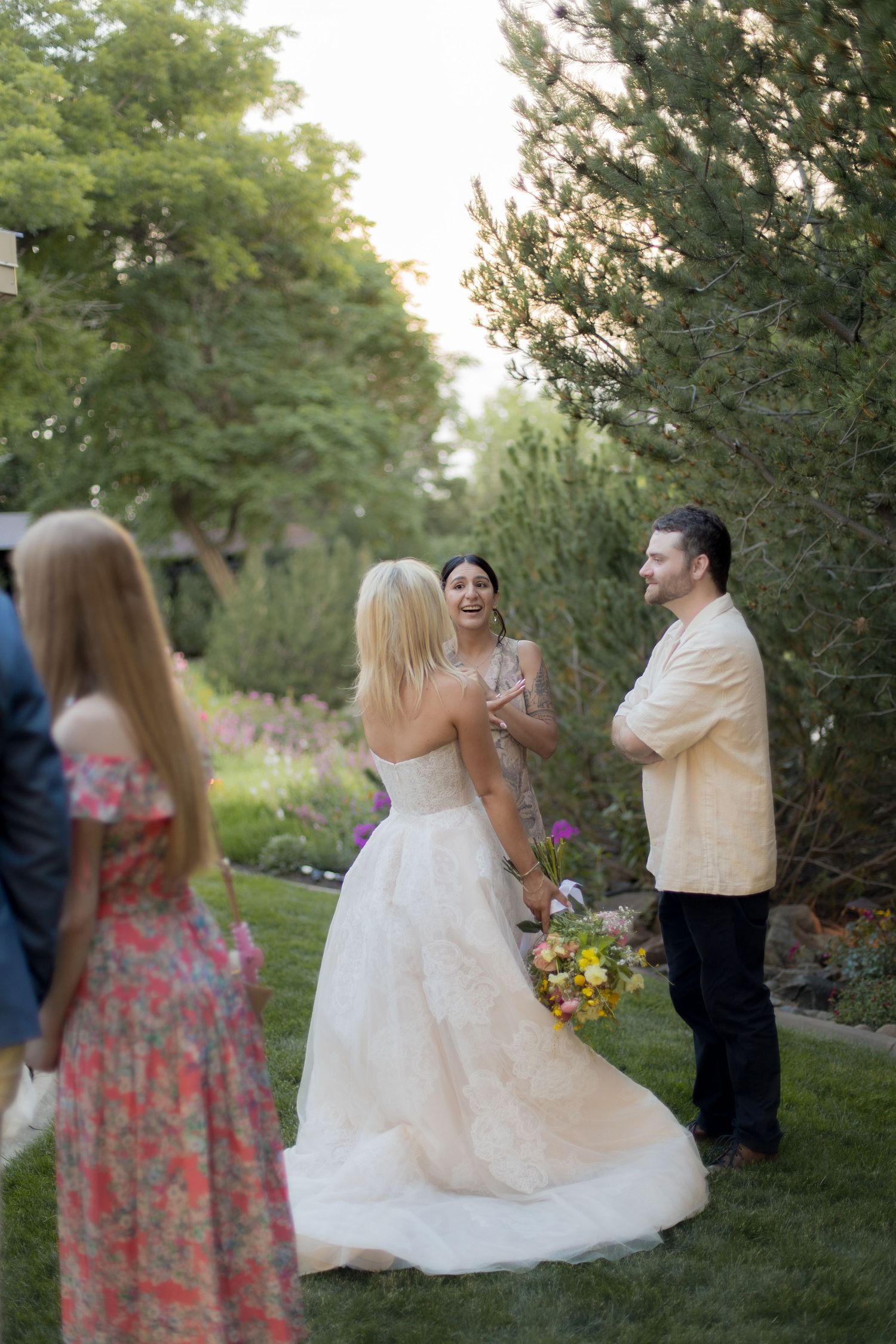 Wedding party celebrates outdoors in a garden setting with bridesmaids in coral dresses and a bride in white gown.