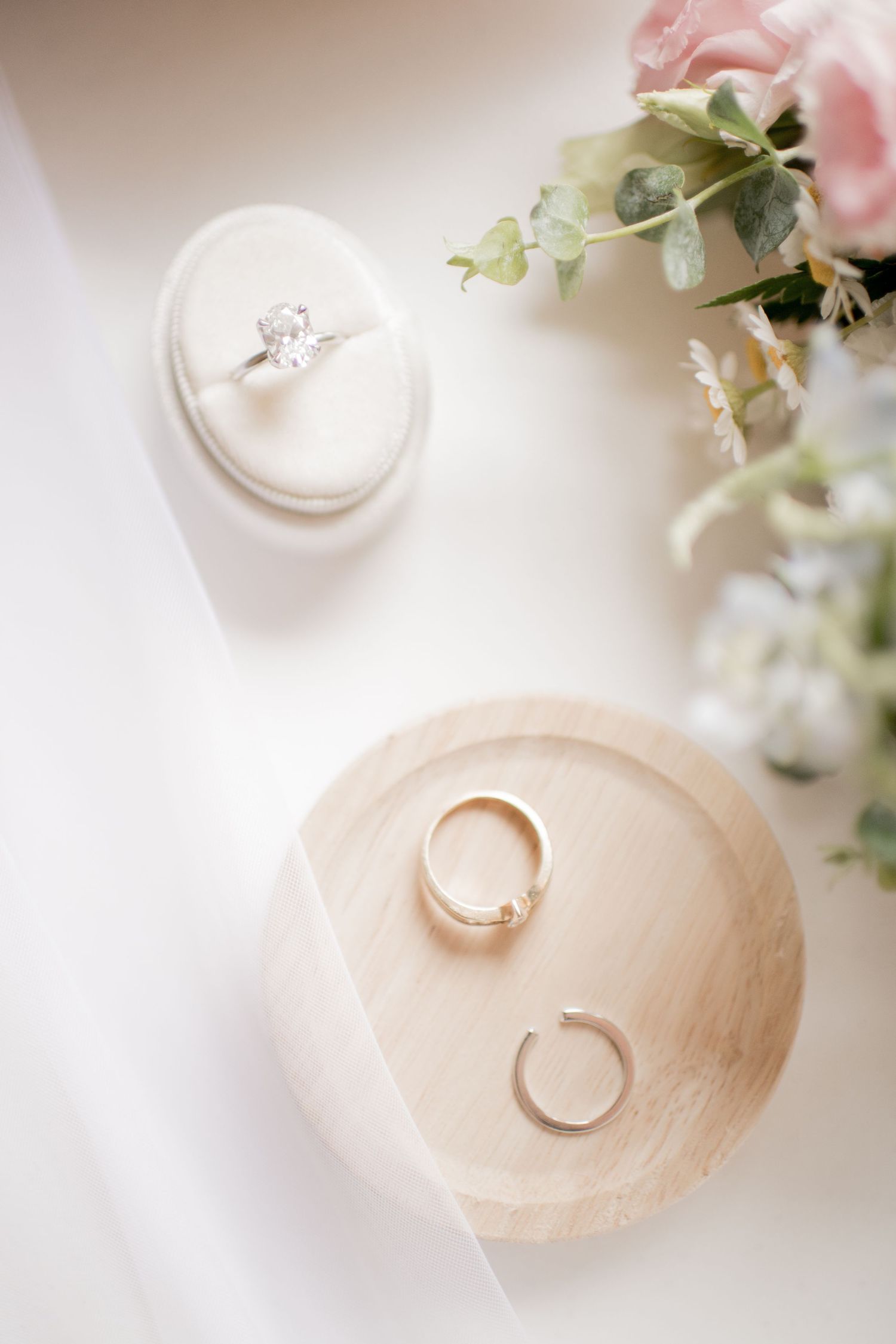 Wedding rings displayed on elegant cream-colored ring holders with soft floral decor and natural lighting.