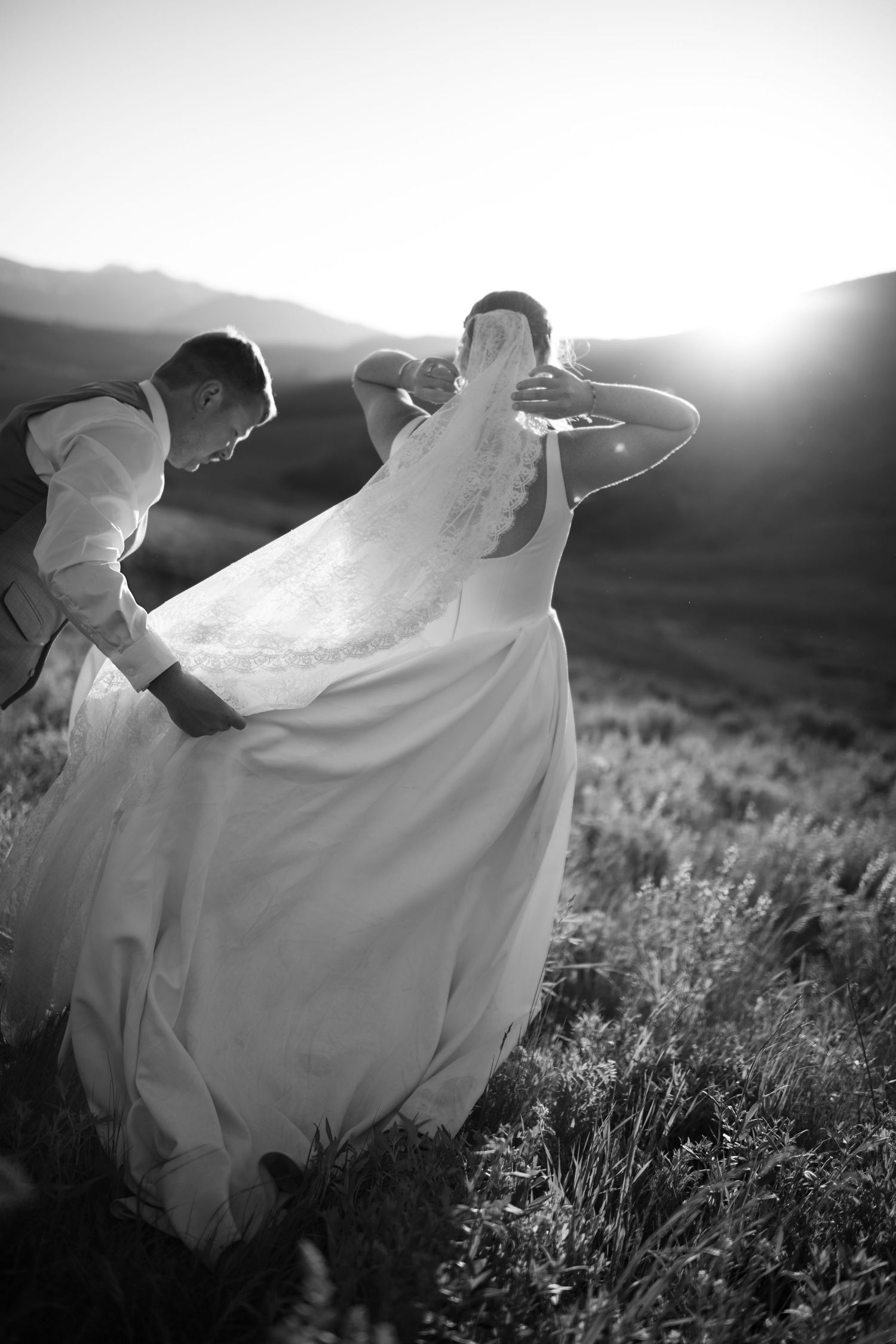 A flowing white wedding dress billows elegantly in the wind against a mountain landscape at sunset.
