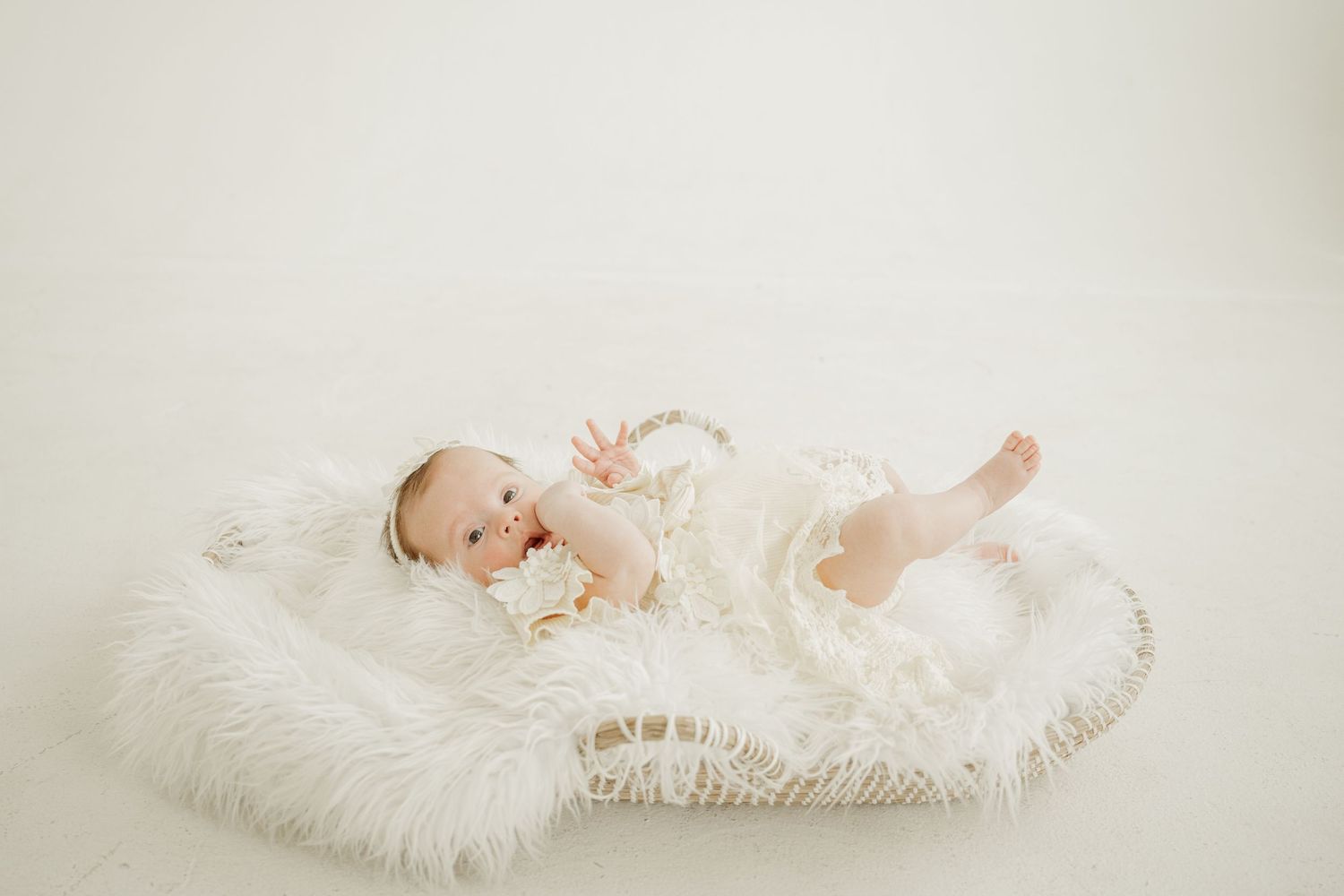 A sleeping newborn baby wrapped in soft white blankets and lace on a light beige background.