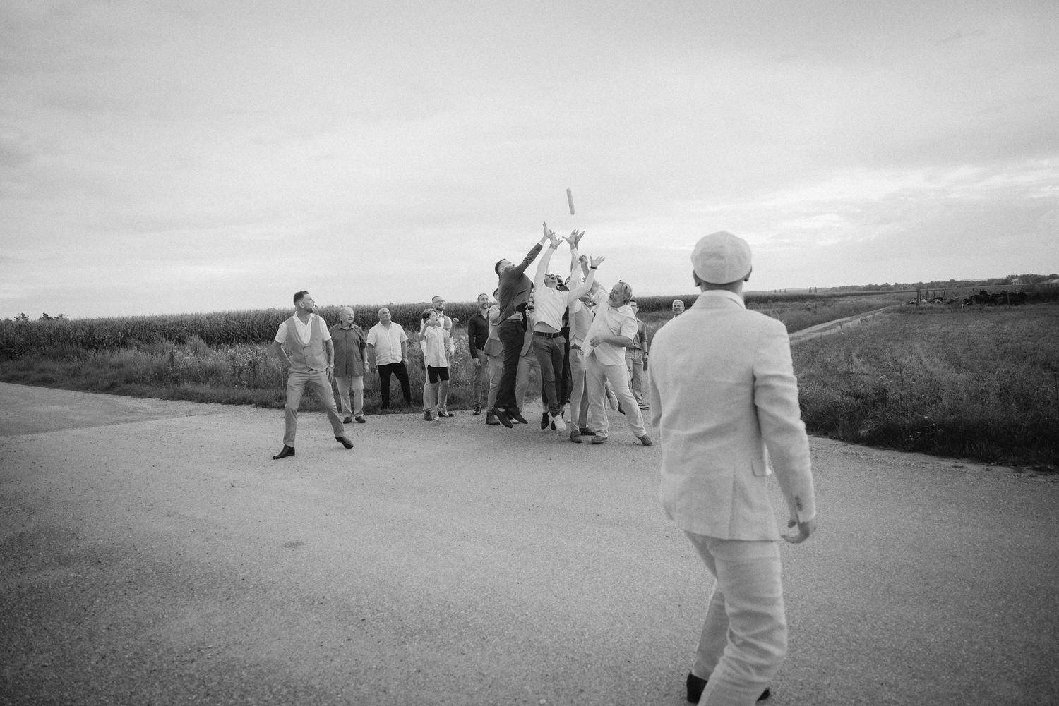 Black and white photo of a group of men celebrating on a rural road, with one person raising their arms in joy.