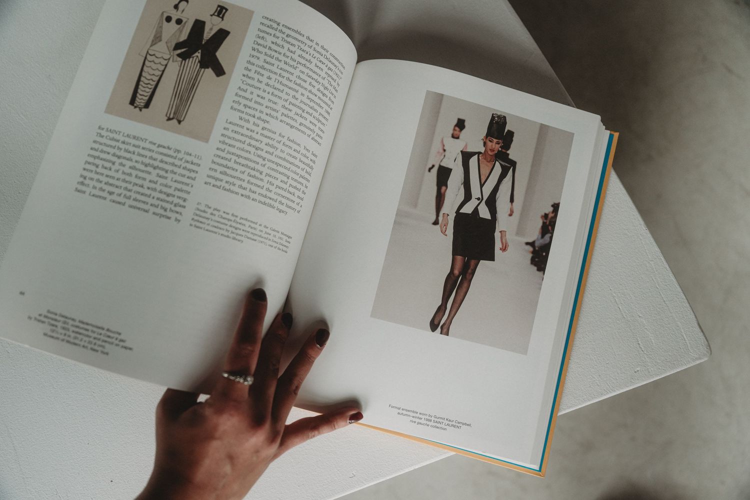 Hand flipping through pages of a fashion design book showing sketches and clothing illustrations.