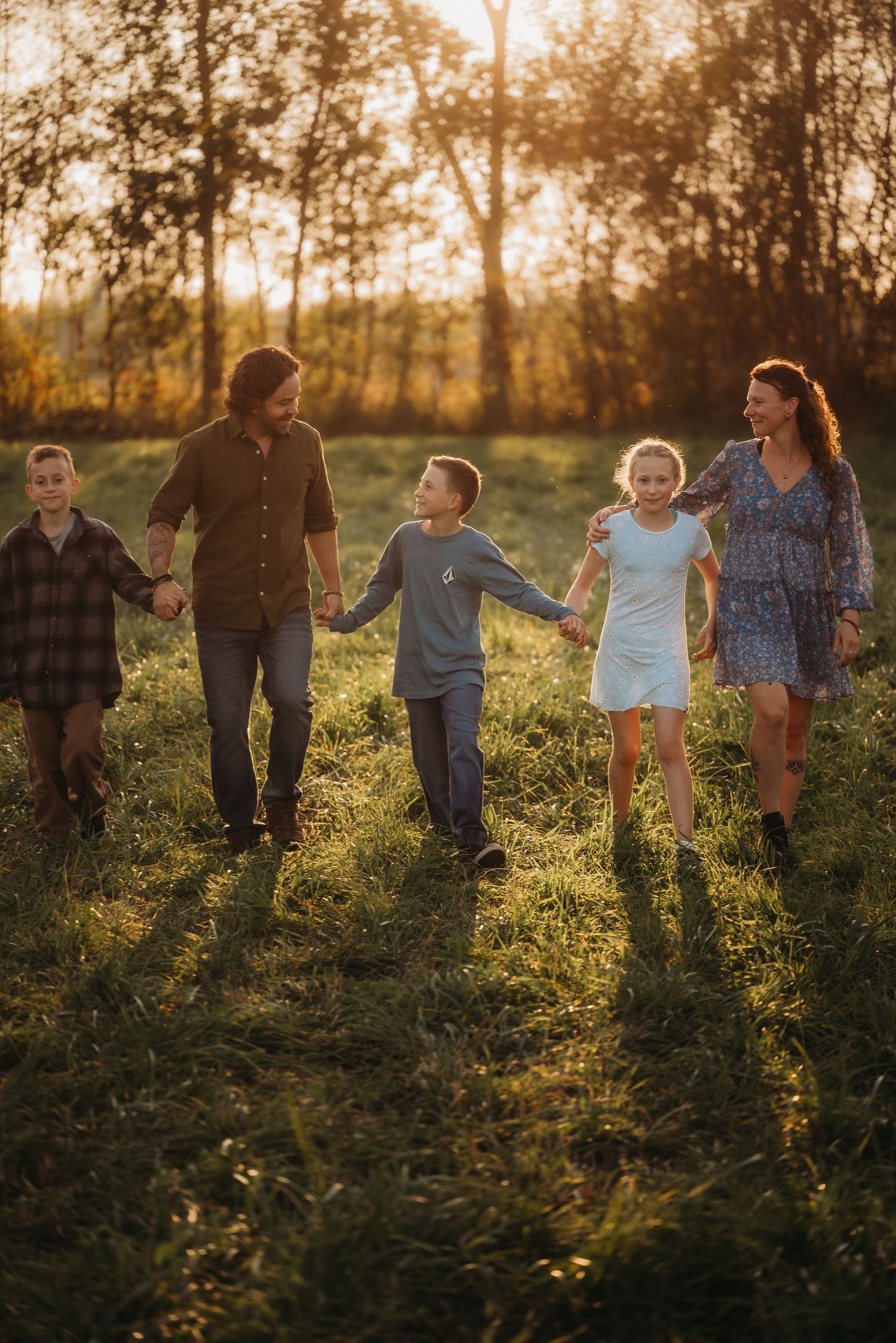 Family walks together holding hands through sun-lit meadow at golden hour.