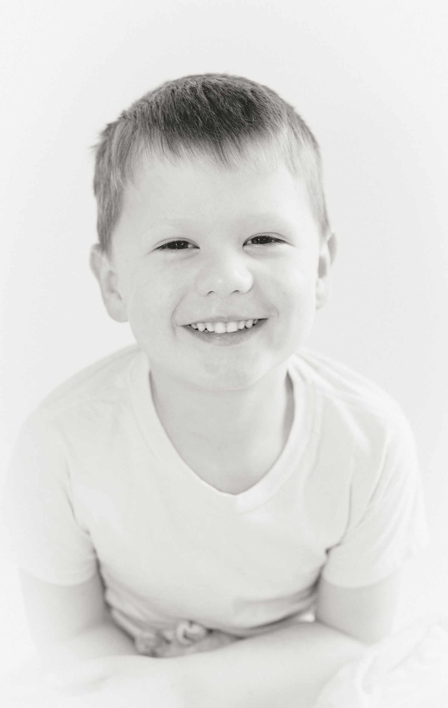 A series of four black and white portraits of a young child in white clothing showing joyful expressions against a light background.