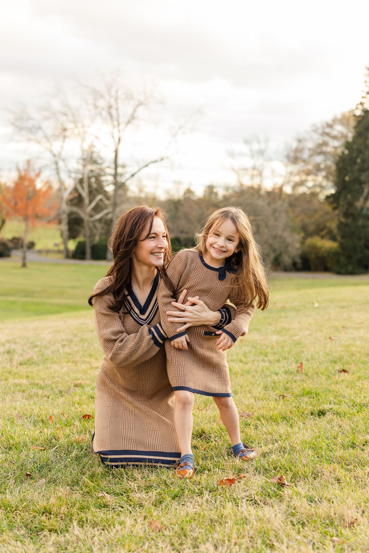 Two friends laugh and play together while sitting in a grassy field on an autumn afternoon.