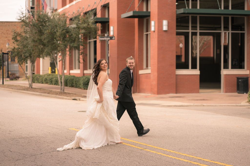 Newlyweds walking together along a brick building exterior.