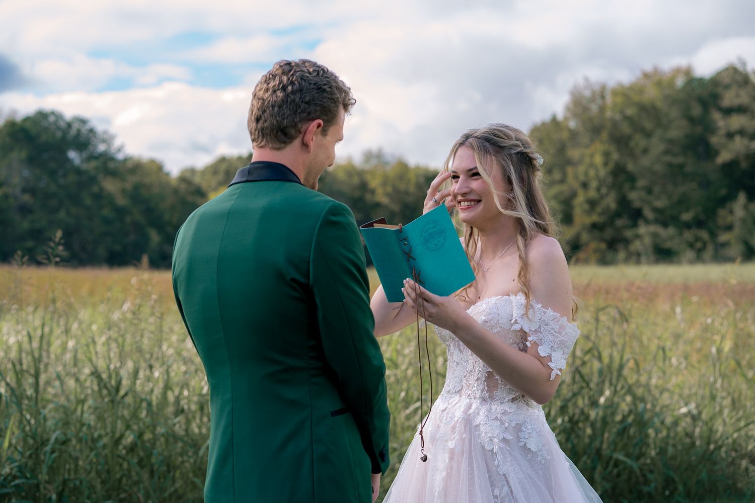 Wedding couple embracing in a sunny field with natural outdoor backdrop.