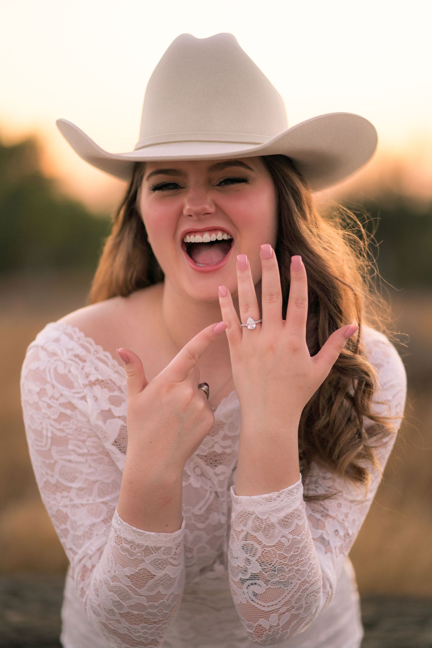 A woman in lace shows off her engagement ring while wearing a cowboy hat.