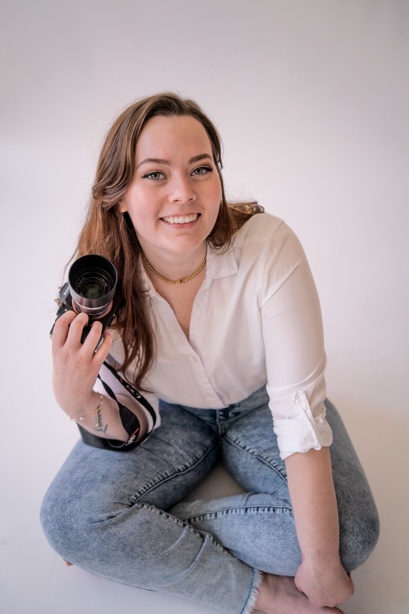 A photographer in casual attire poses with camera equipment against white background.
