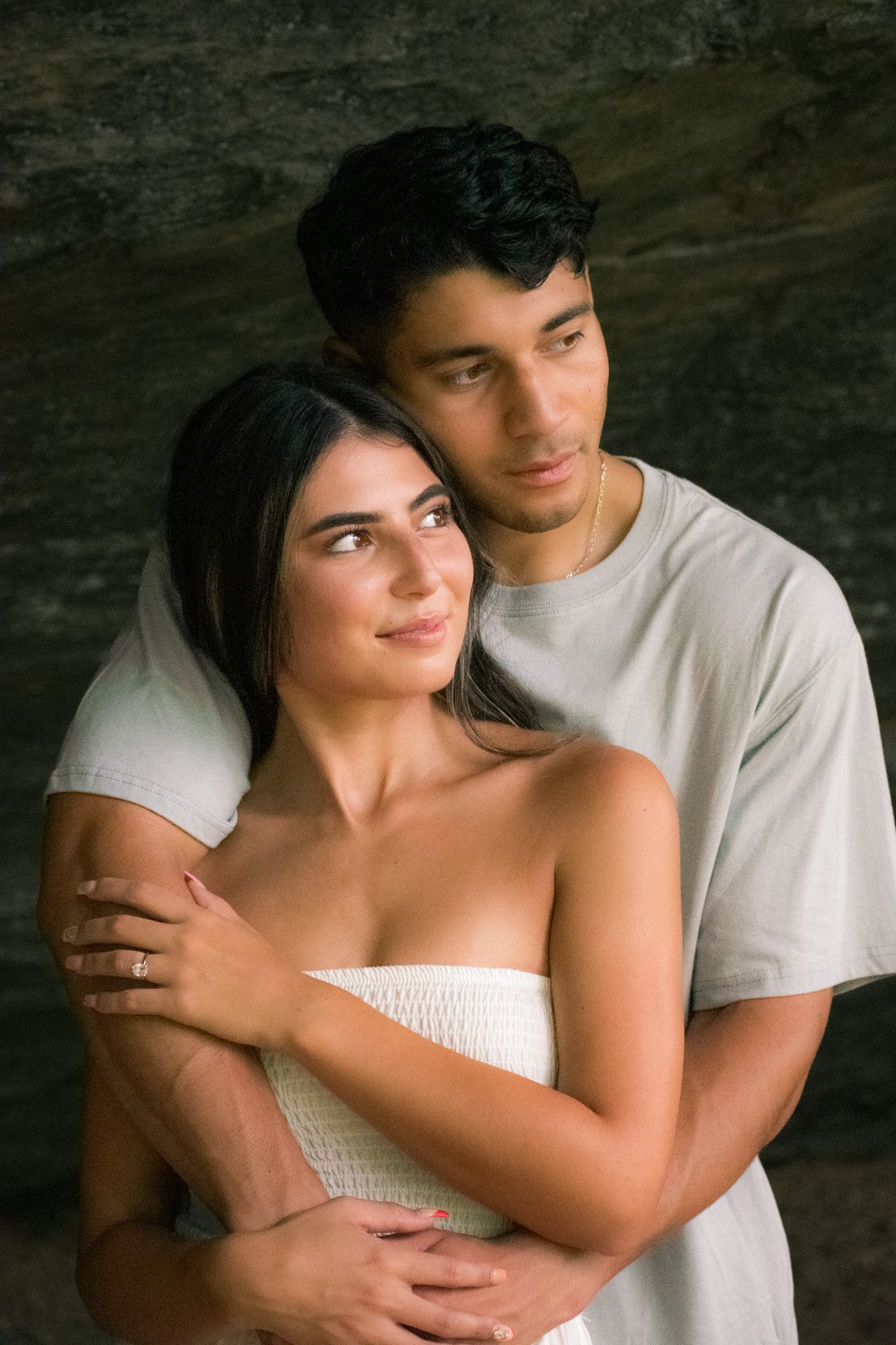A romantic couple embraces in casual white clothing against a dark background.