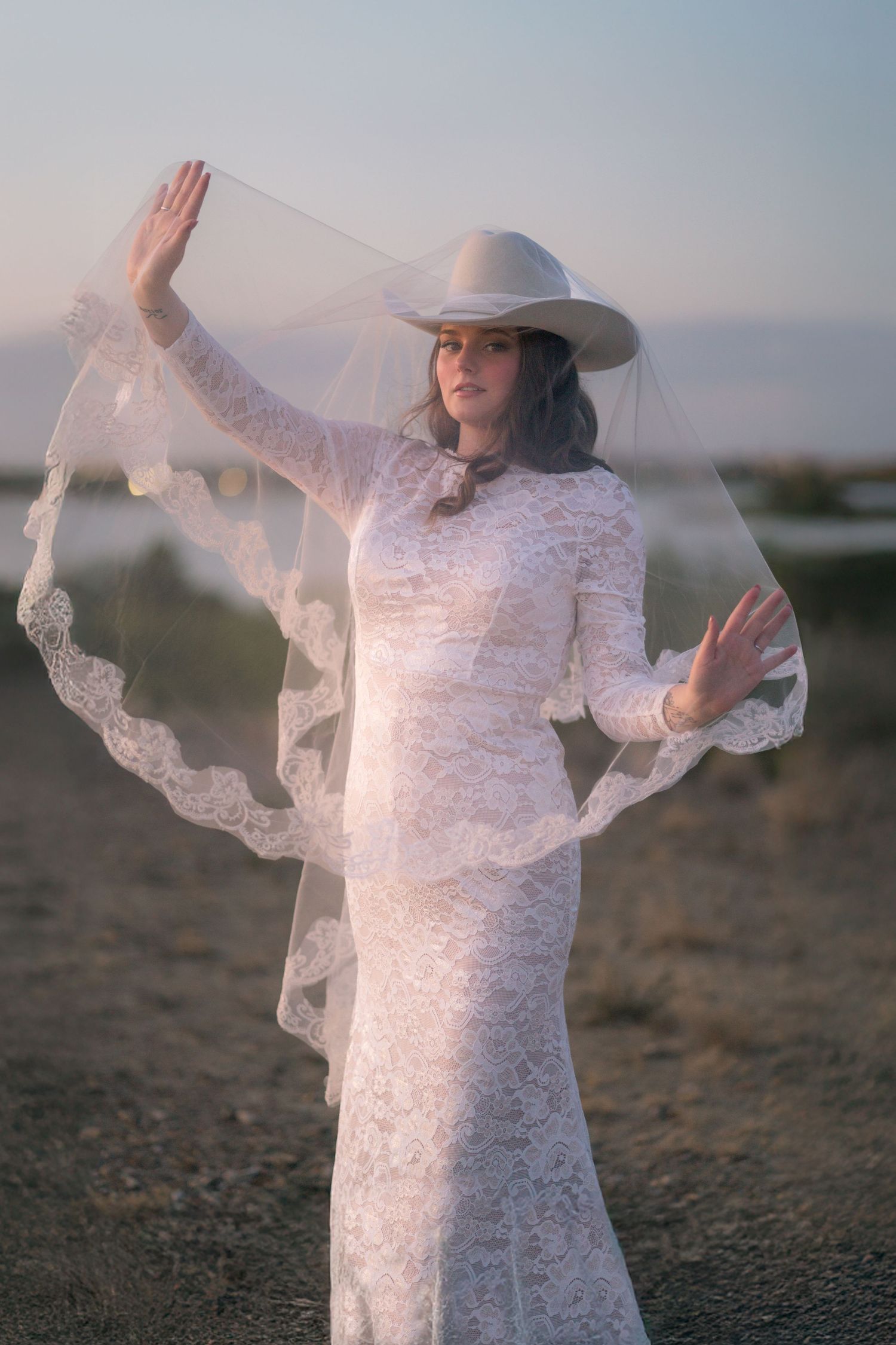 Ethereal bridal portraits in white lace dress and hat against misty backdrop.