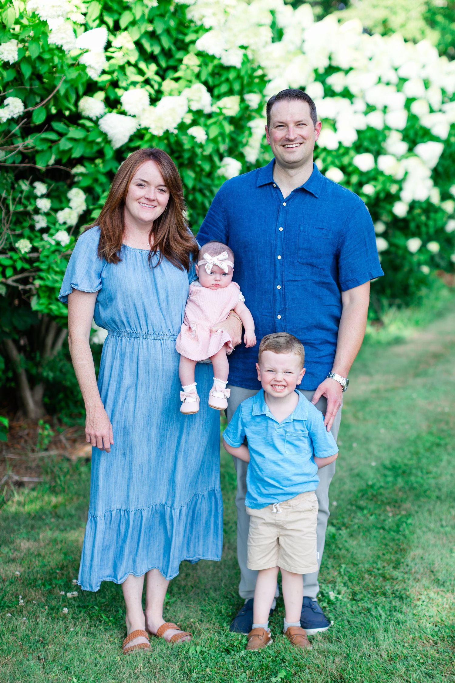 A family poses together in a garden setting wearing coordinating blue outfits on a sunny summer day during a photo session