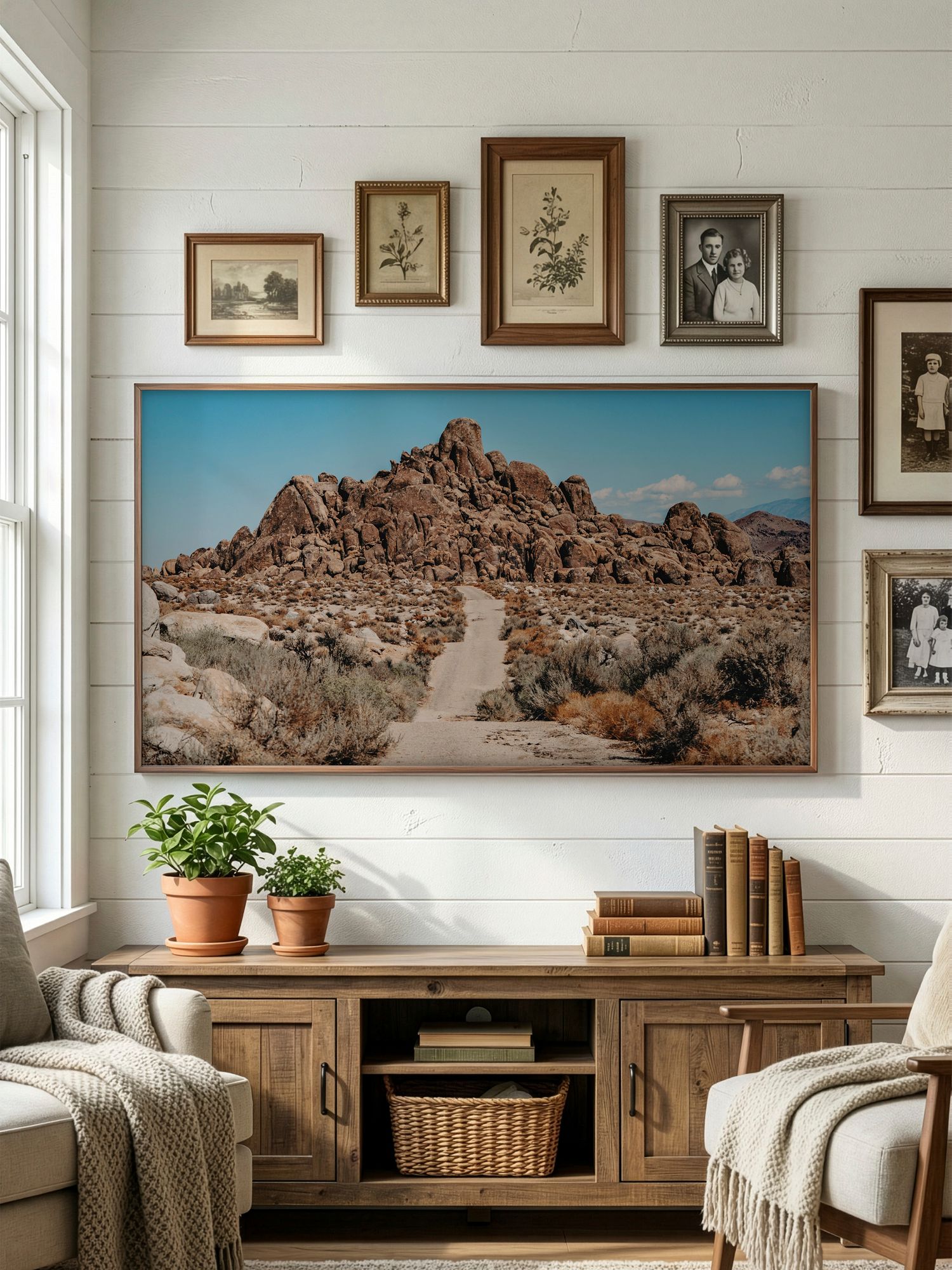 A desert landscape photograph displayed above a wooden media console with vintage frames and potted plants in a cozy room.