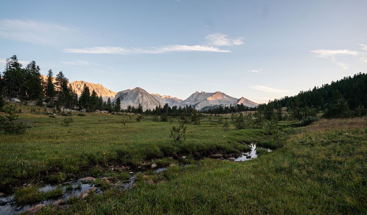 Sweeping mountain vista with green meadows and distant peaks under blue skies.