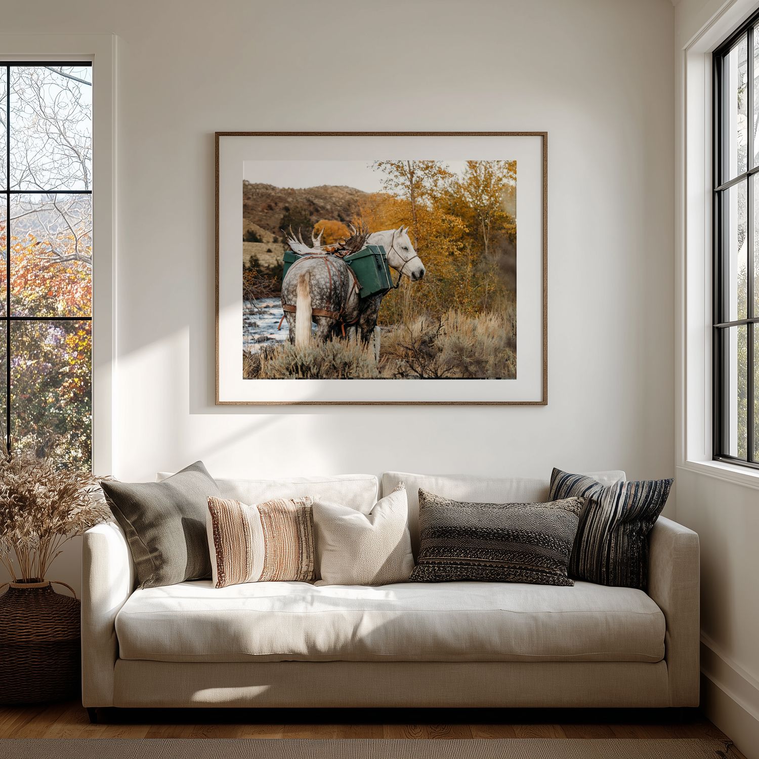 A framed western-style photograph of horses in an autumn landscape hangs above a cream colored sofa with throw pillows.