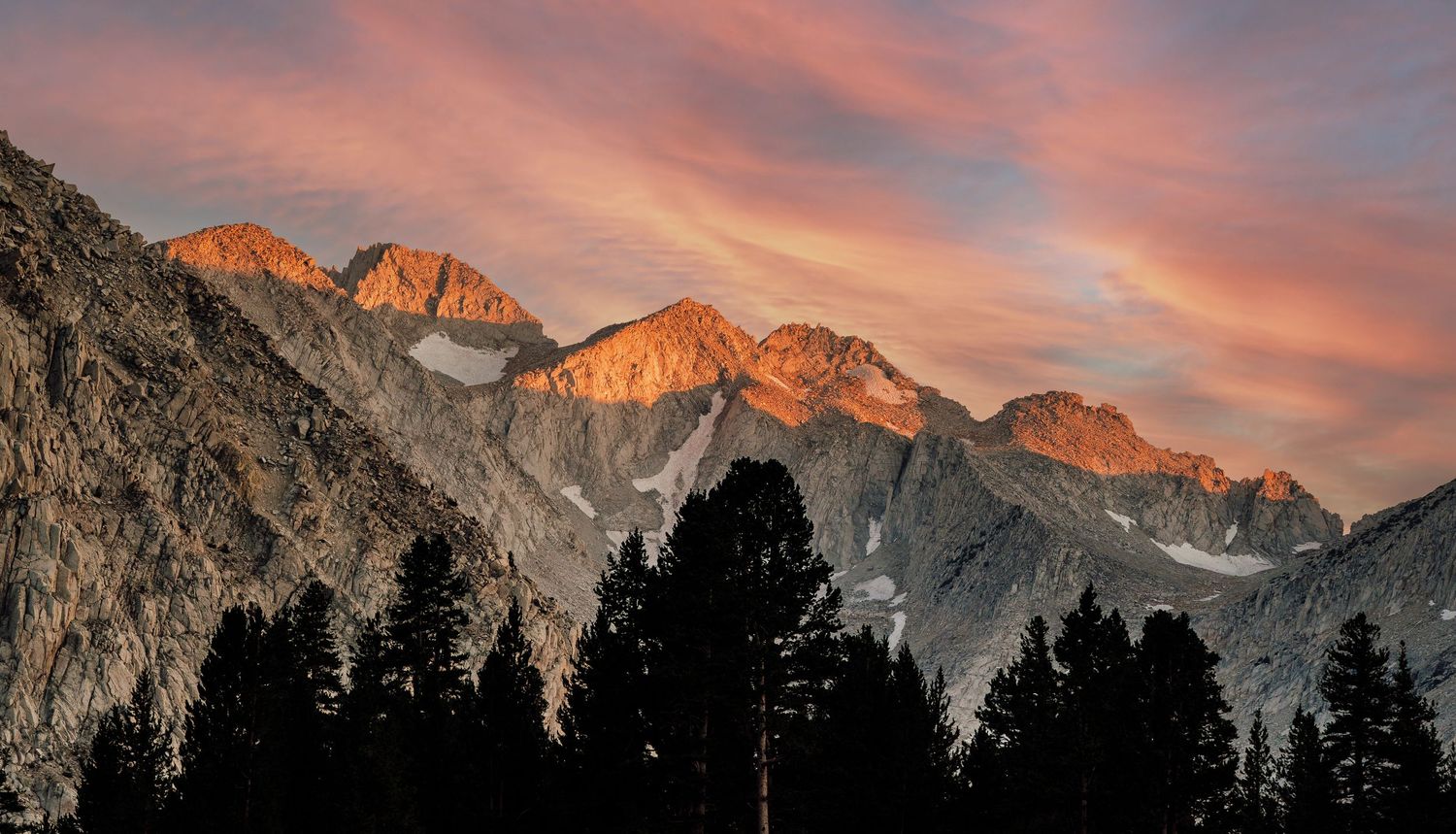Dramatic sunset illuminates mountain peaks with vibrant orange alpenglow against a purple sky.