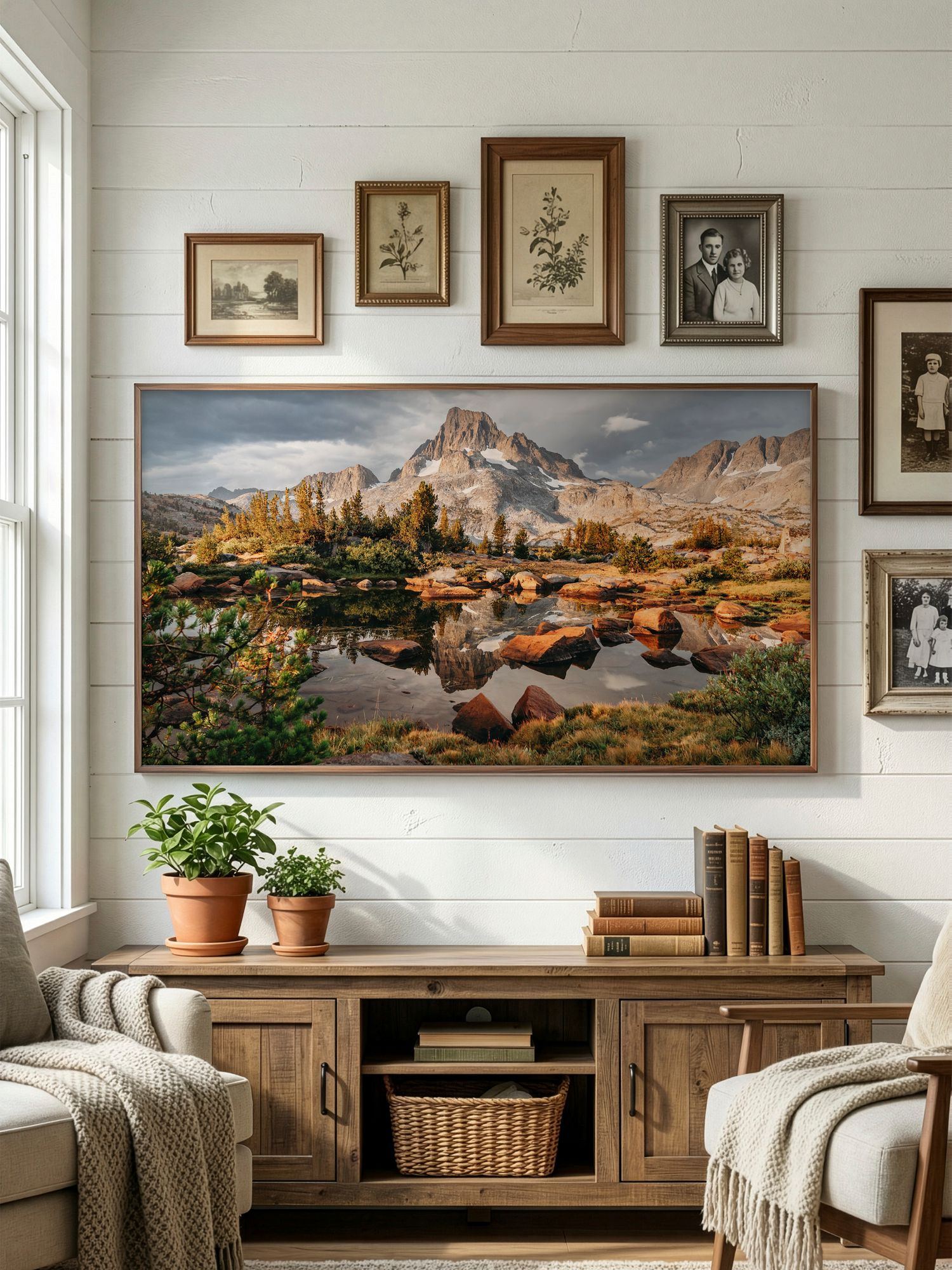 A cozy living room features a large landscape photograph of mountains above a wooden media console with potted plants and artwork.