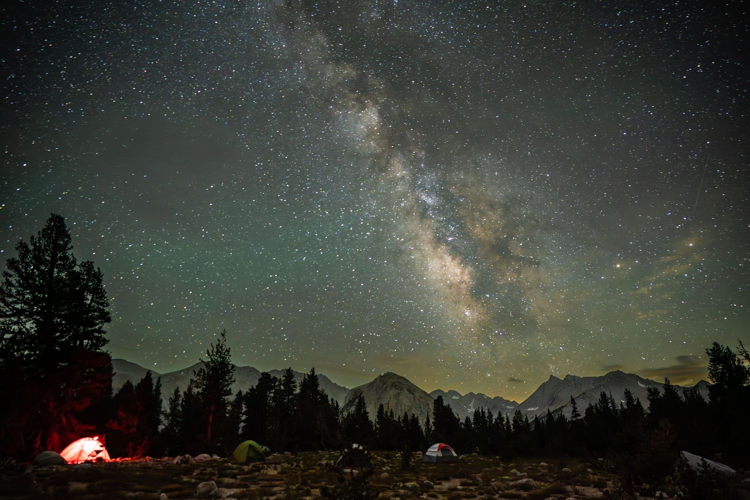 Milky Way galaxy stretches across night sky over silhouetted mountain landscape.
