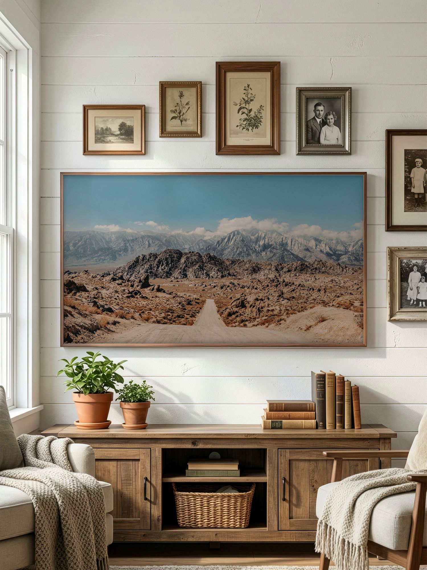 A cozy living room interior with panoramic desert landscape artwork and vintage framed photos on white shiplap walls.
