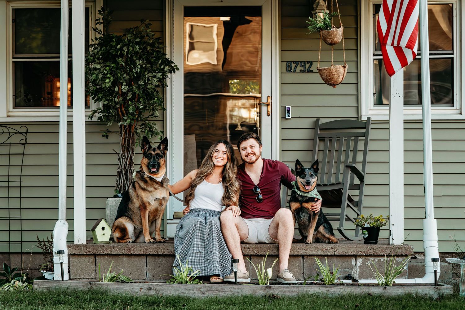 Dogs and owners relaxing on front porch of house with American flags.