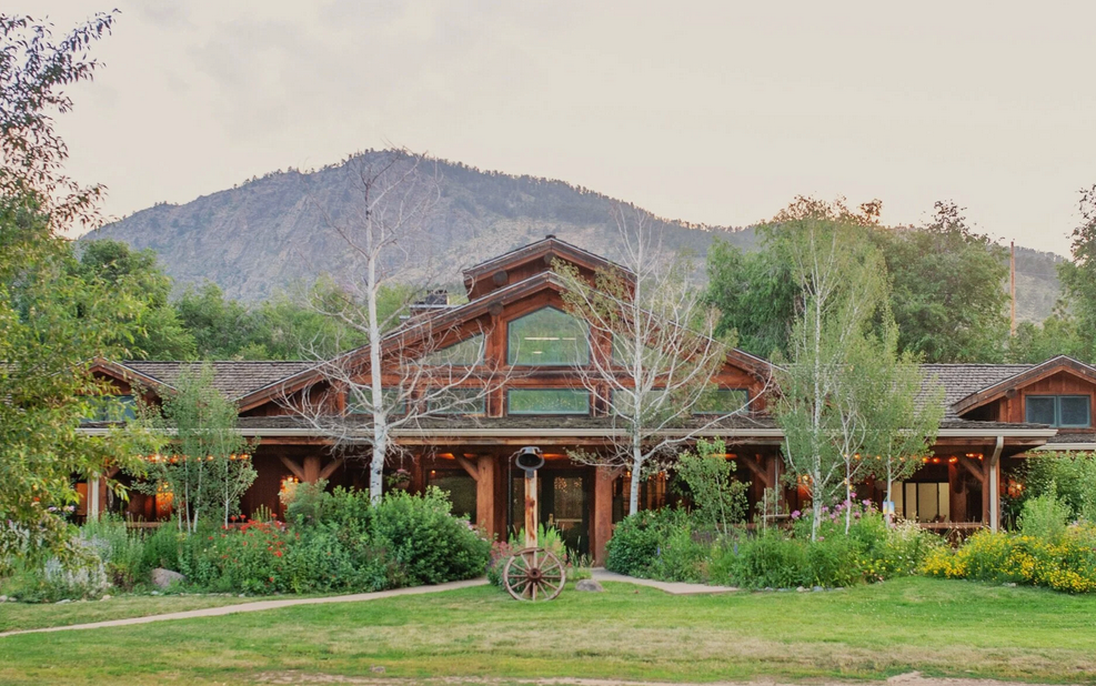 Rustic log cabin buildings nestled in a mountain valley with green landscaping.