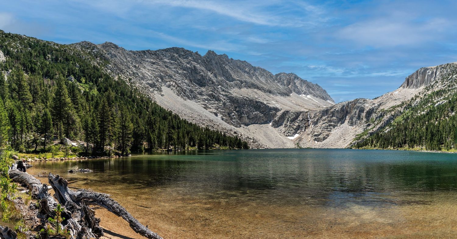 Crystal clear alpine lake reflects surrounding mountain peaks under bright blue skies.