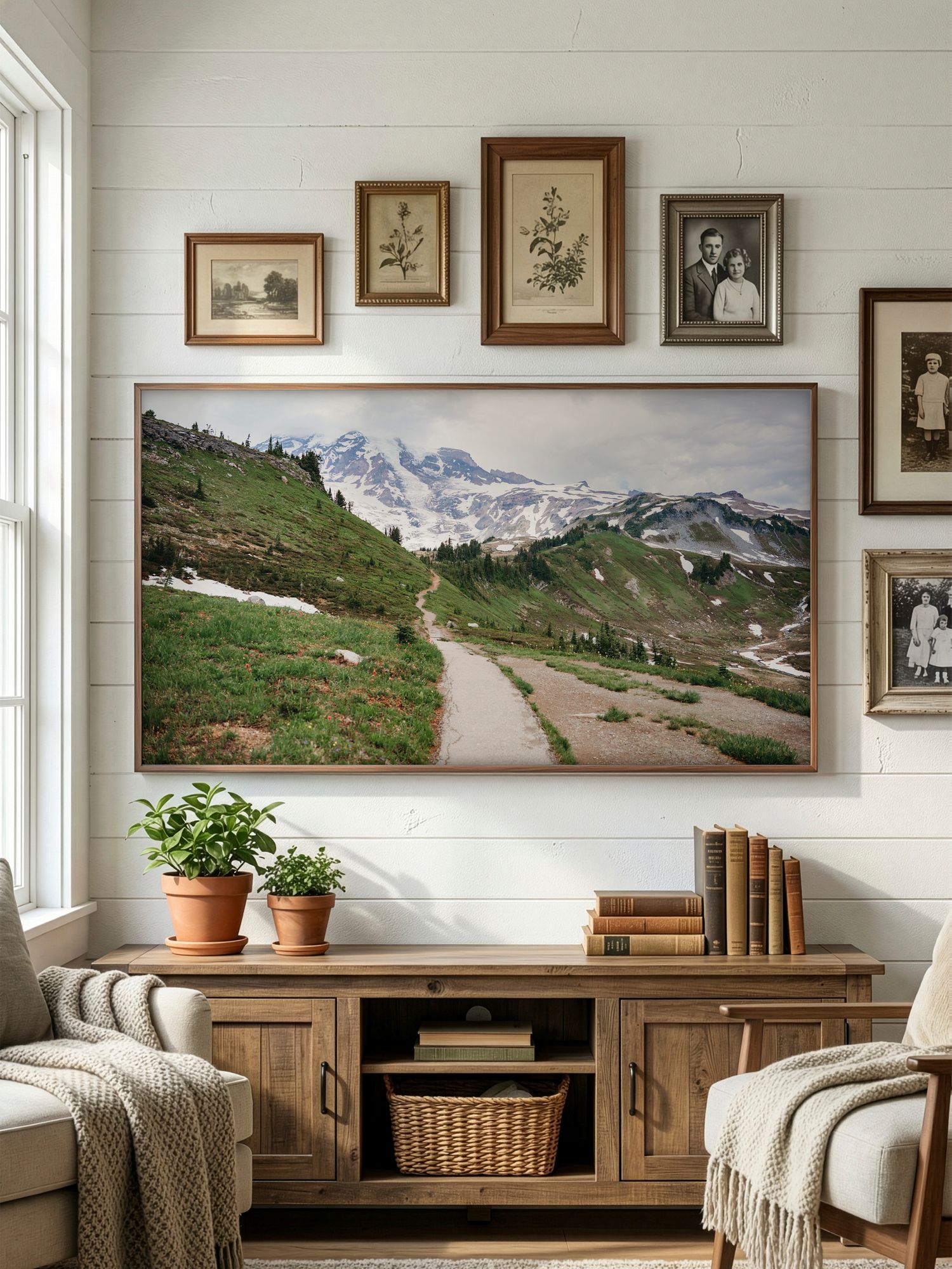 Panoramic mountain landscape artwork displayed above wooden console in cozy living room with neutral decor and potted plants.