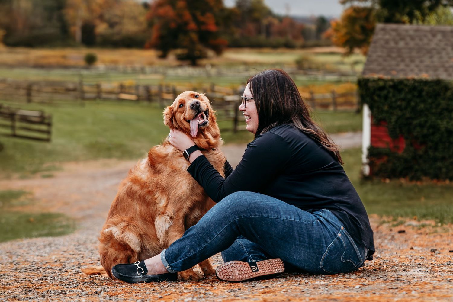 Golden retriever and person sitting together on autumn leaves during a cozy outdoor photoshoot.
