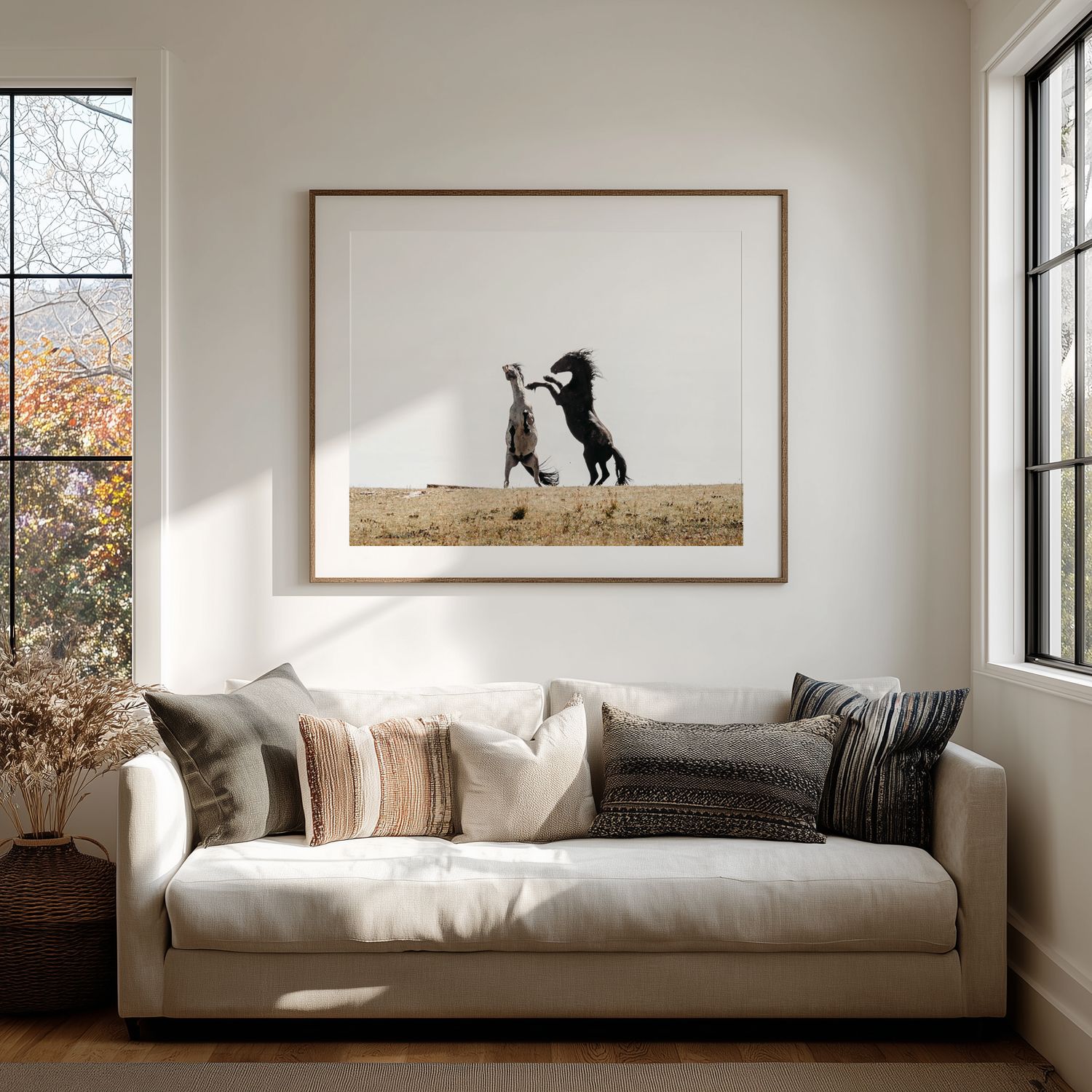 A black cat sits on a white couch by a window in a minimalist room with natural lighting.