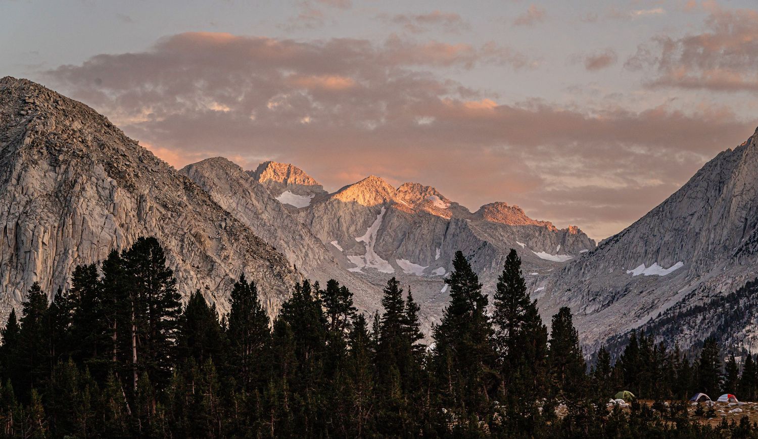 Mountain peaks glow with warm sunset colors against a cloudy evening sky.