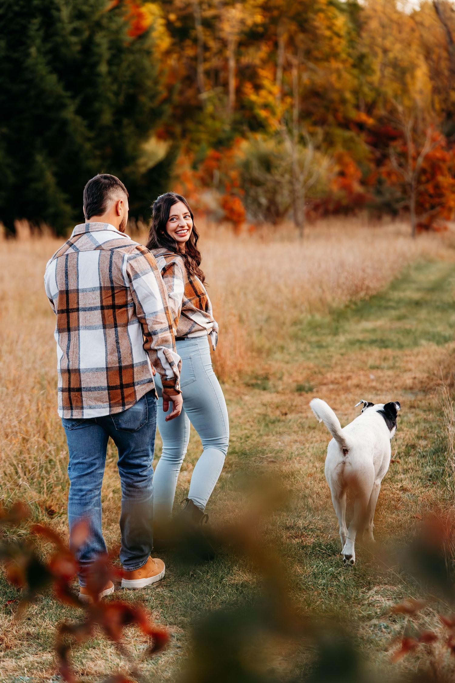 A couple and their white dog enjoying an autumn day in a golden field.