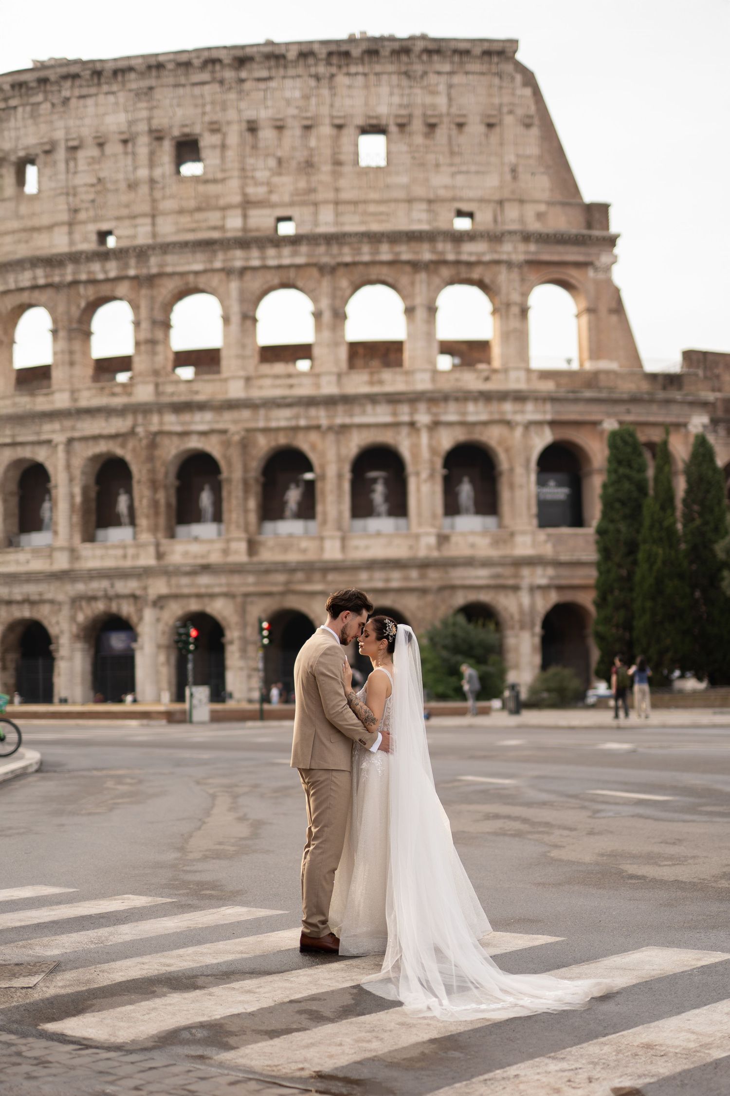Bride and groom share a romantic kiss on a crosswalk in front of the iconic Colosseum in Rome, Italy.