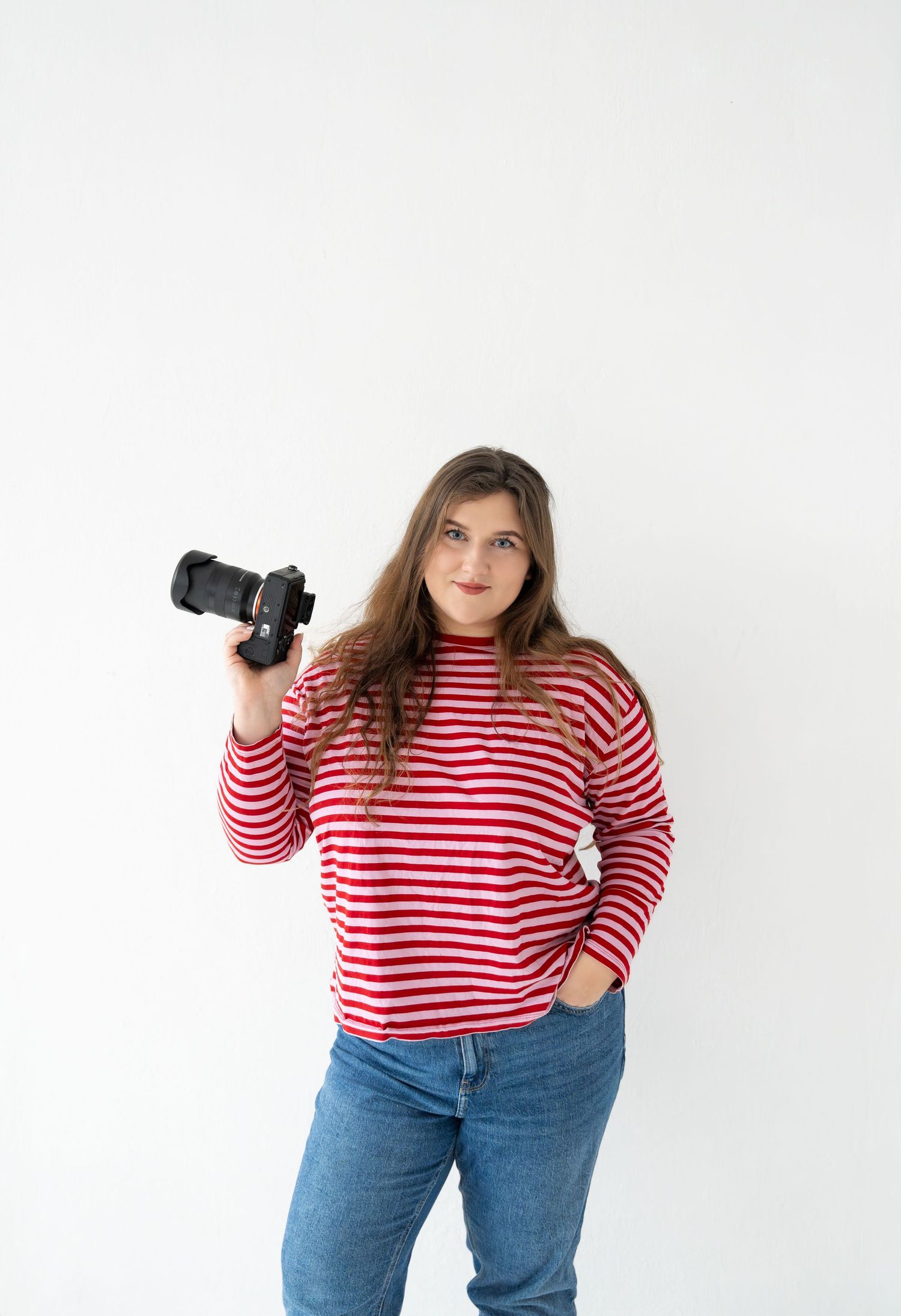 Photographer in red striped sweater holding camera against white background.