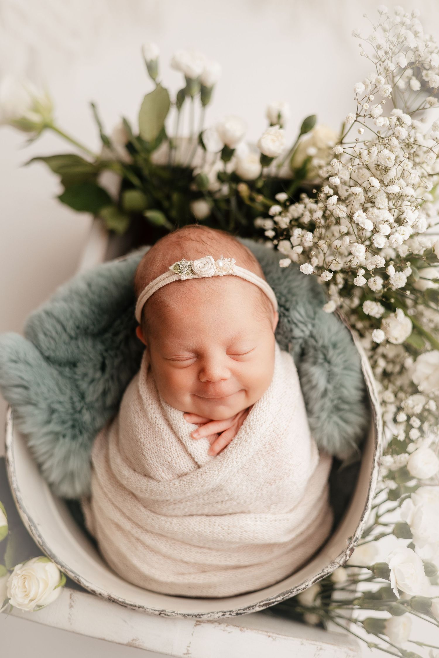 Sleeping newborn wrapped in white swaddle with baby's breath flowers and greenery.