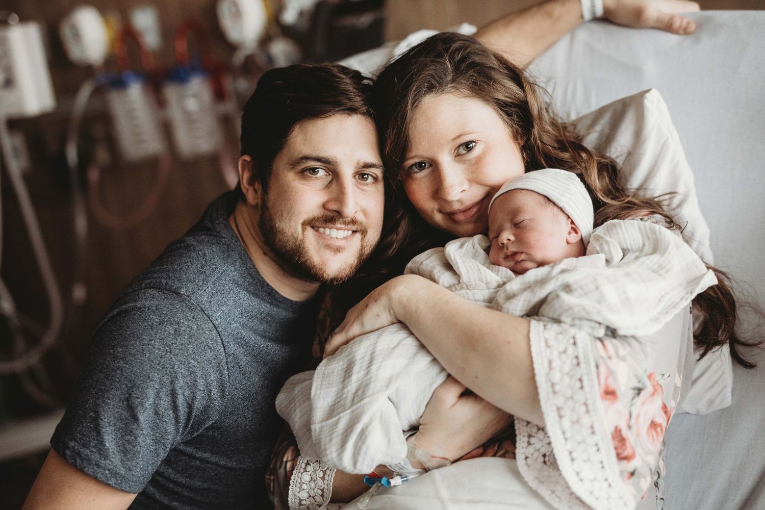 Parents snuggle with their newborn baby in a cozy hospital room setting.