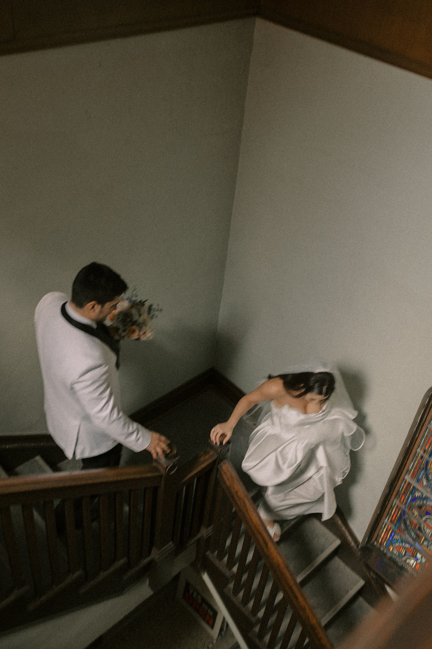 Artistic wedding photo of couple sharing private moment on dark wooden staircase.