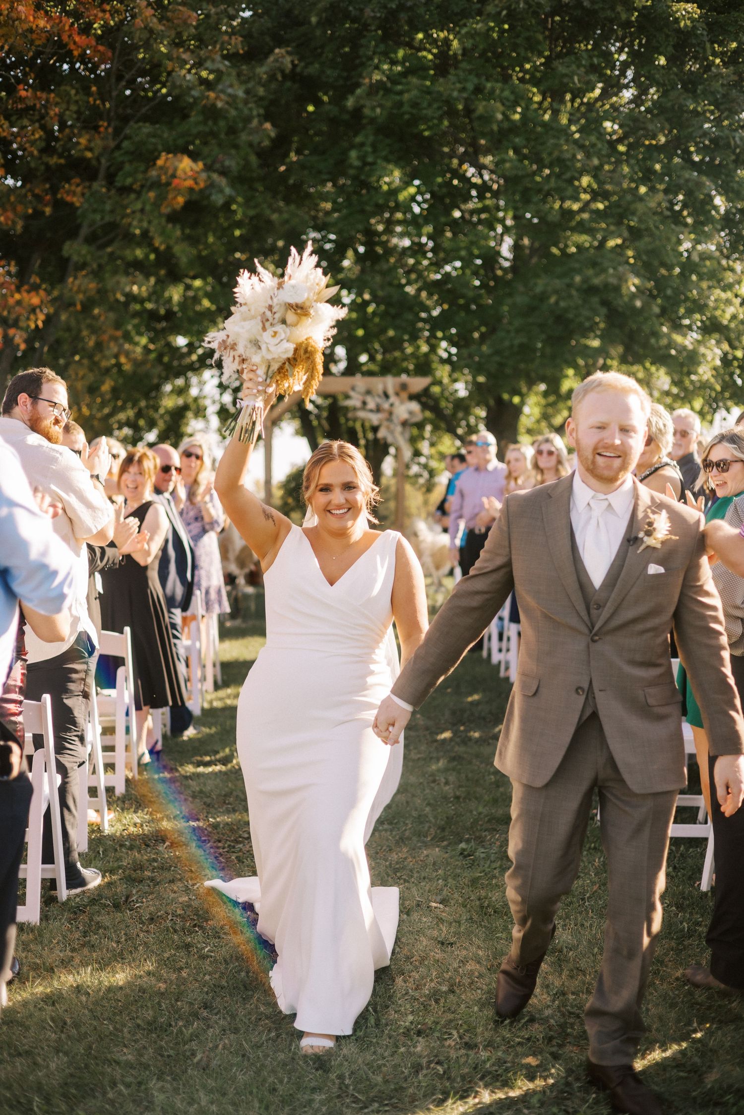 A joyful couple walks down the aisle after their outdoor wedding ceremony while guests cheer.