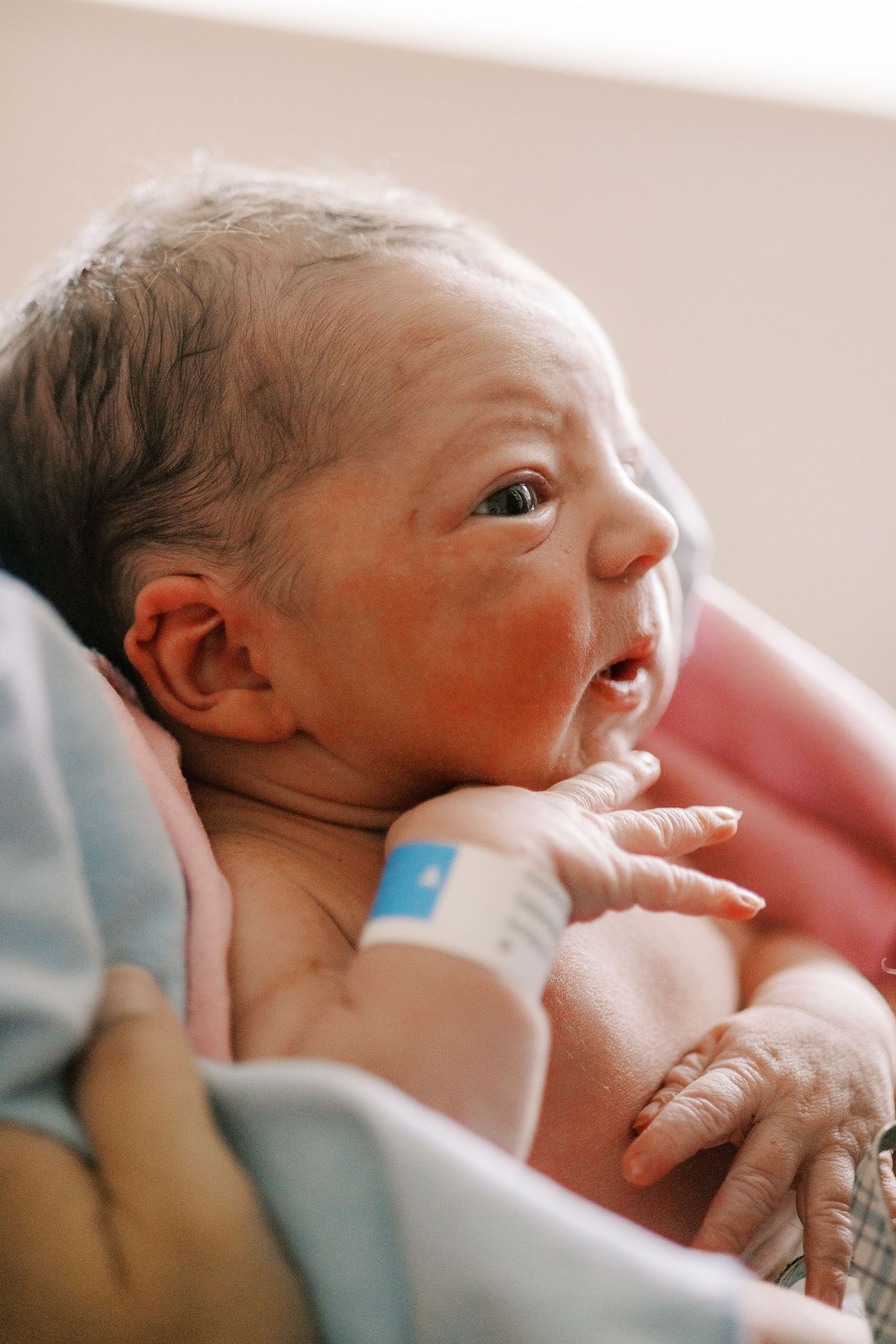Close-up portrait of a newborn baby with rosy cheeks wearing a hospital bracelet.