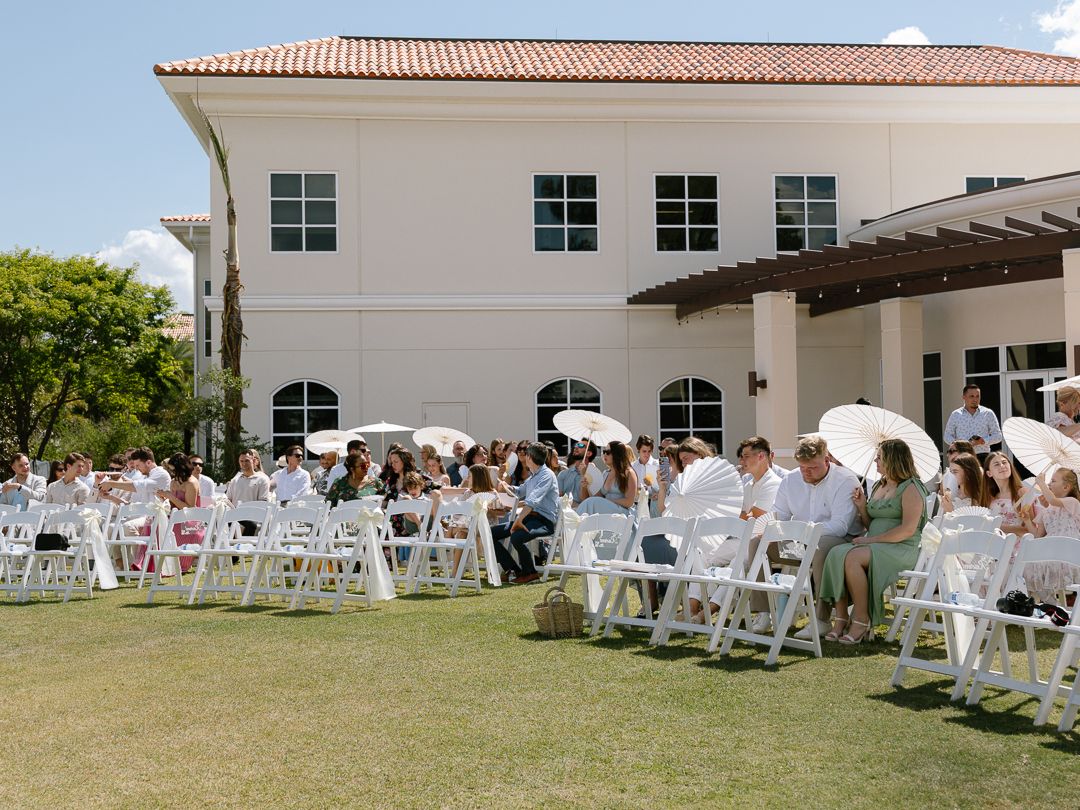 Guests seated in white chairs on a lawn for an outdoor wedding ceremony at an elegant venue.