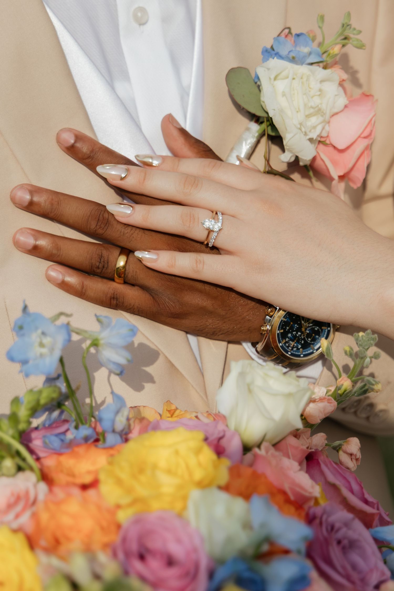 Close-up of newlyweds hands showing wedding rings above a vibrant colorful bridal bouquet.