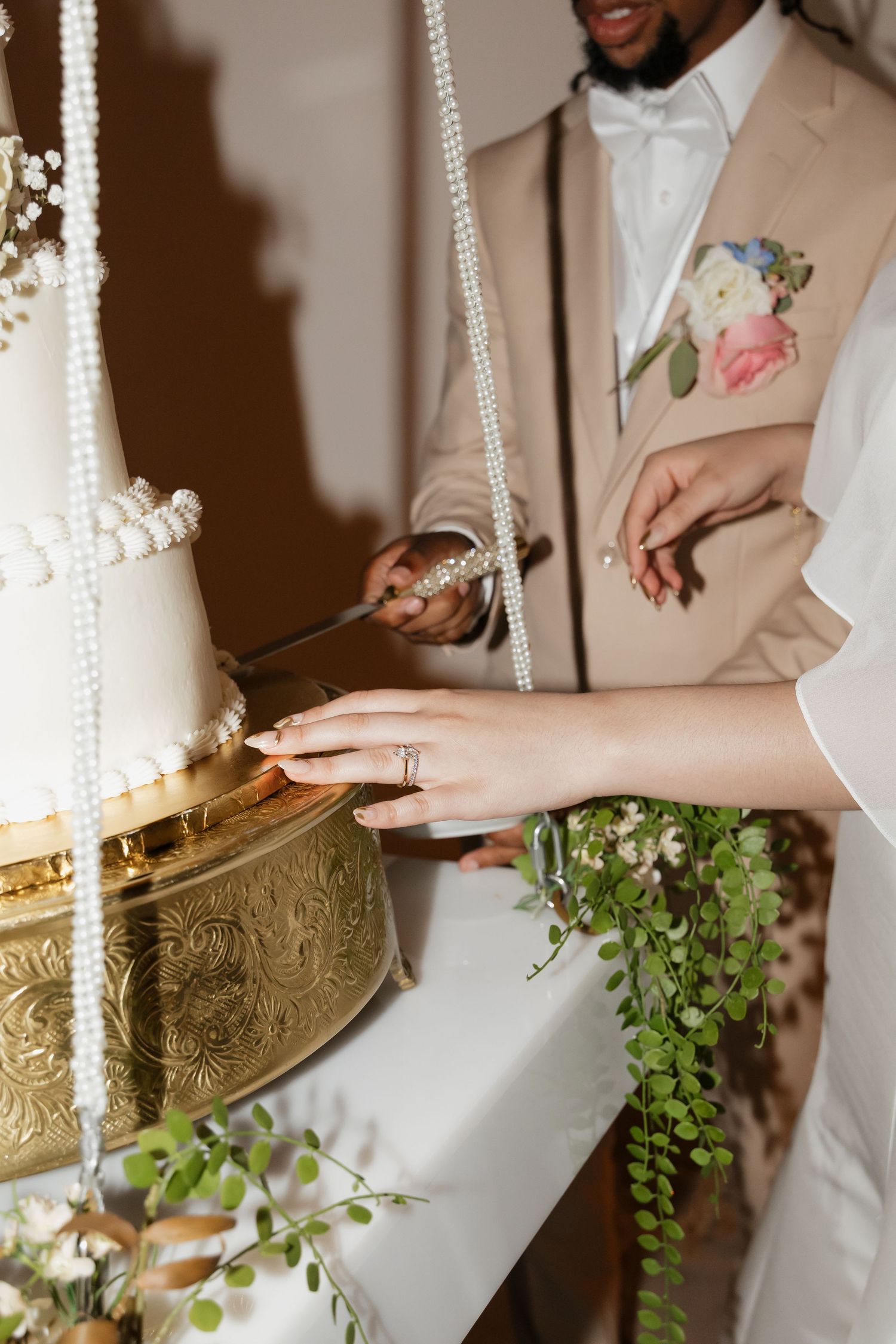 Close-up of bride and groom cutting white tiered wedding cake with pearl strand decorations.