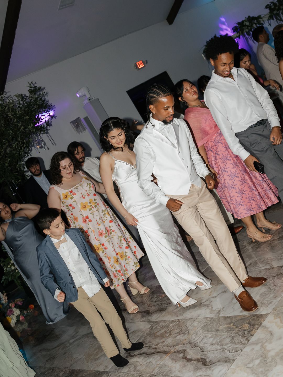 Wedding guests dancing together on the dance floor during a lively indoor wedding reception celebration.
