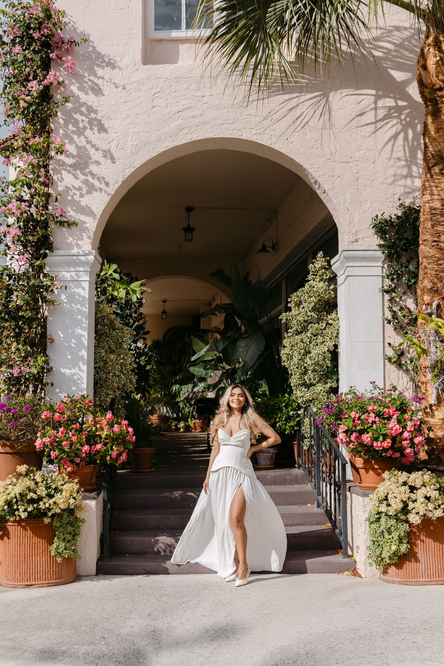Radiant bride in white flowing gown walks through floral archway entrance of elegant venue.