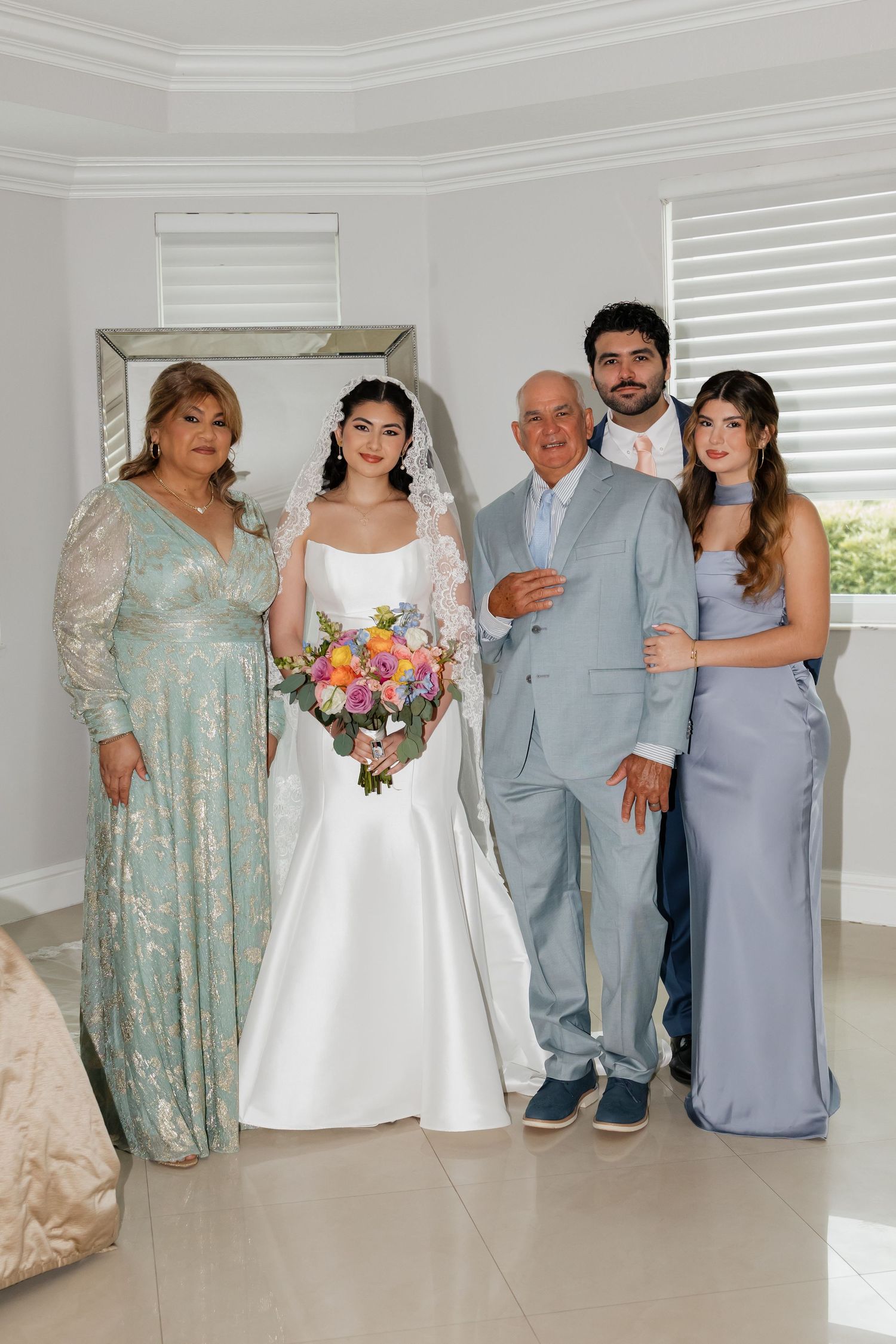 Wedding family portrait with bride in white gown holding colorful bouquet with four relatives.