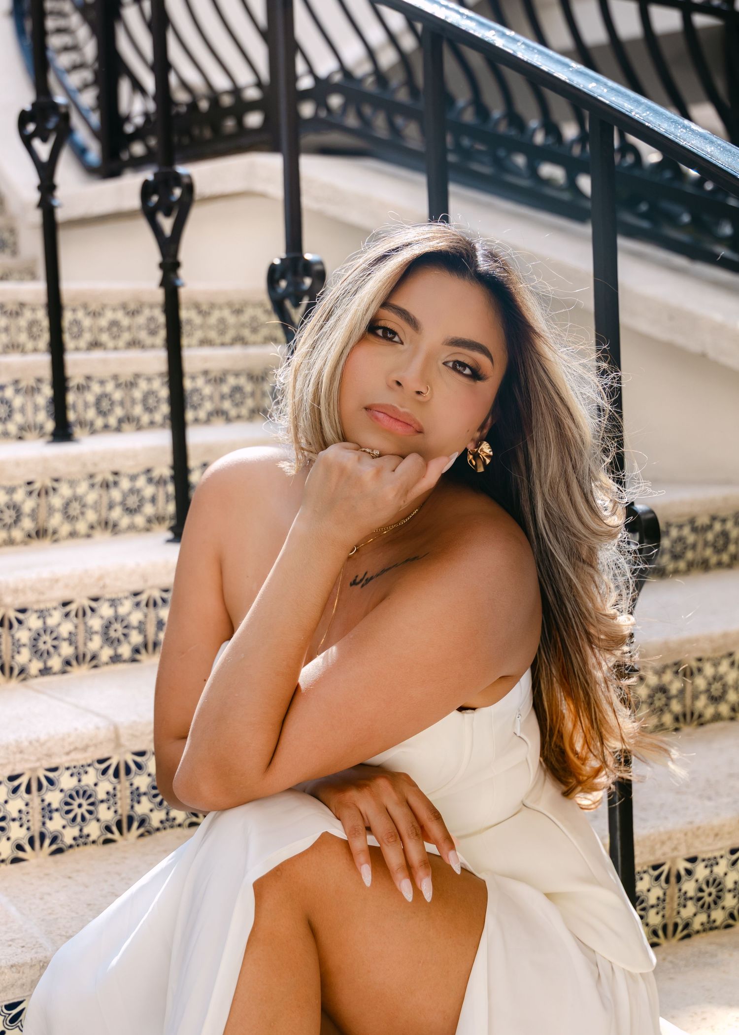 Beautiful bride in strapless white dress sits on decorative tiled steps with ornate iron railing.