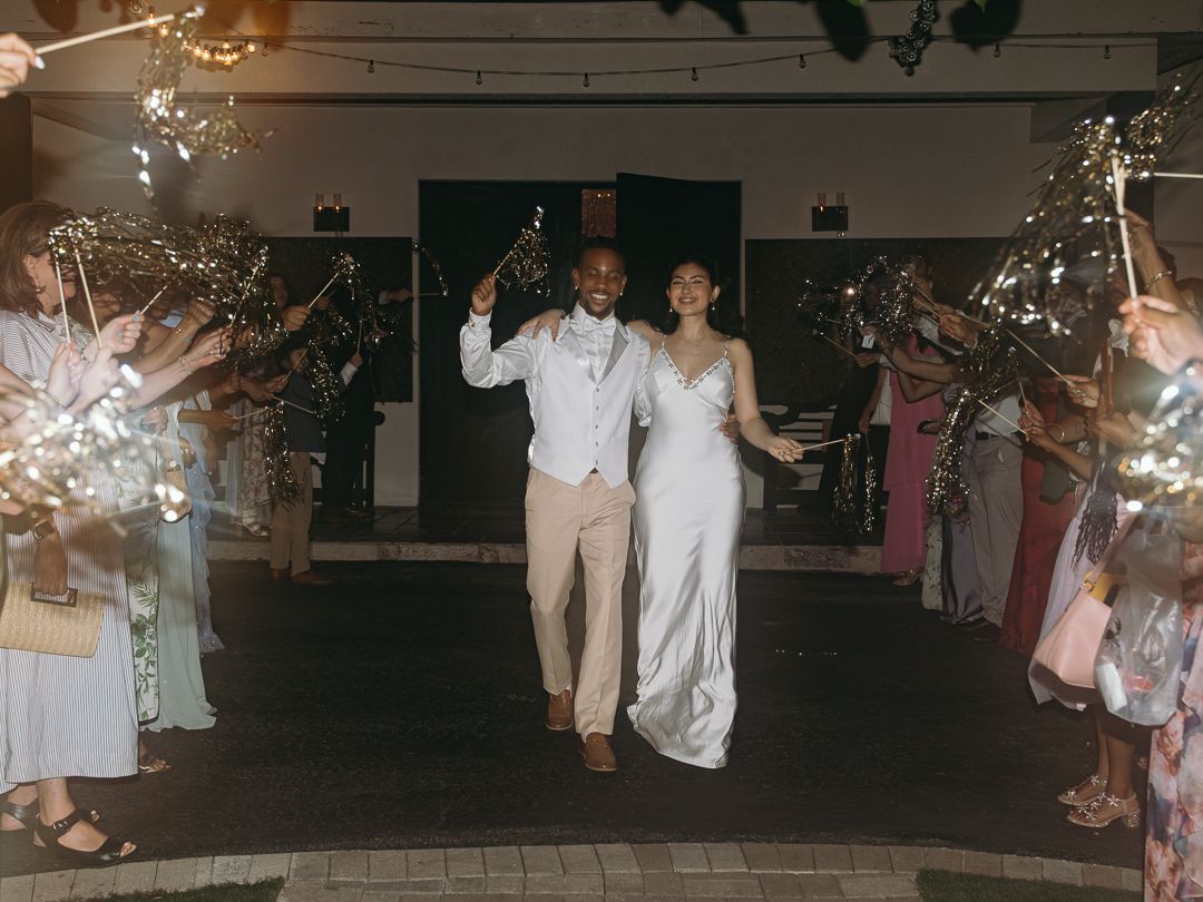 Newlywed couple making a grand sparkler exit surrounded by cheering guests at their wedding reception.